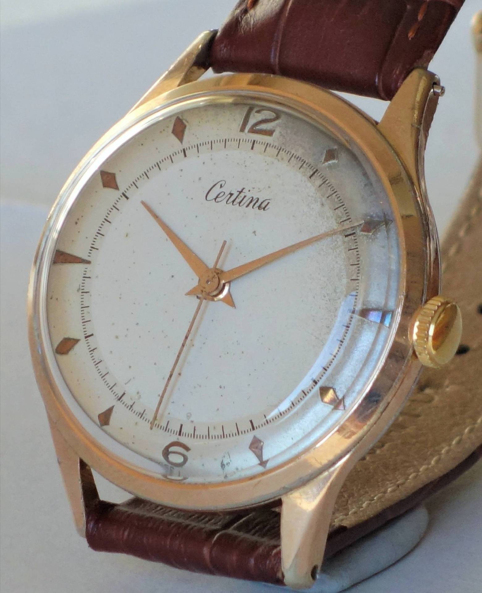 Goldfarbene Certina Armbanduhr mit weißem Zifferblatt und braunem Armband.