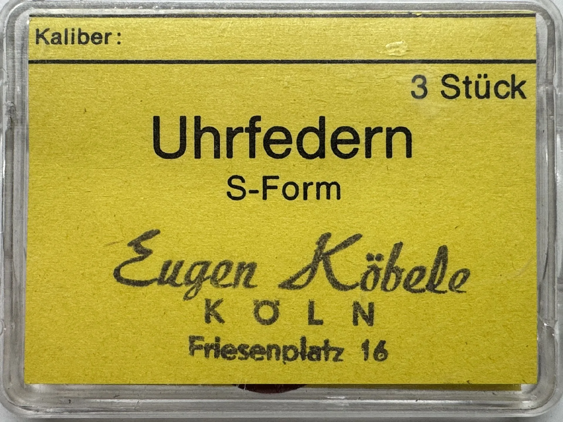 Gelbe Verpackung mit drei S-förmigen Uhrfedern als Ersatzteile.