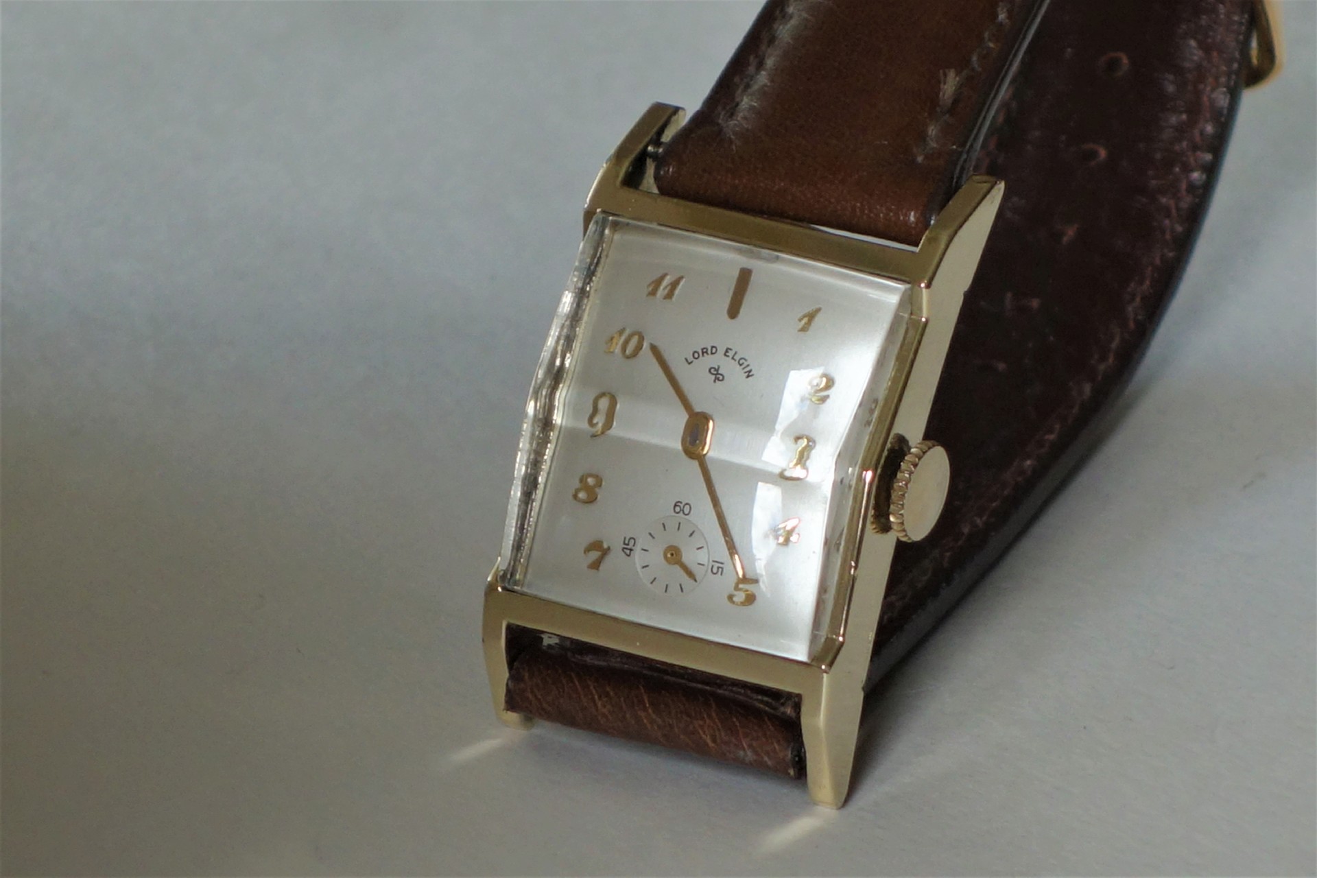 Rechteckige Armbanduhr mit braunem Armband und hellem Zifferblatt.