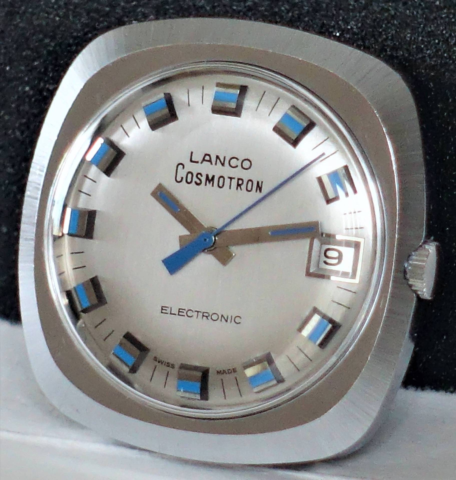 Silberfarbene Armbanduhr mit eckigem Gehäuse und blau-silbernen Indizes, Datumsanzeige bei drei Uhr.
