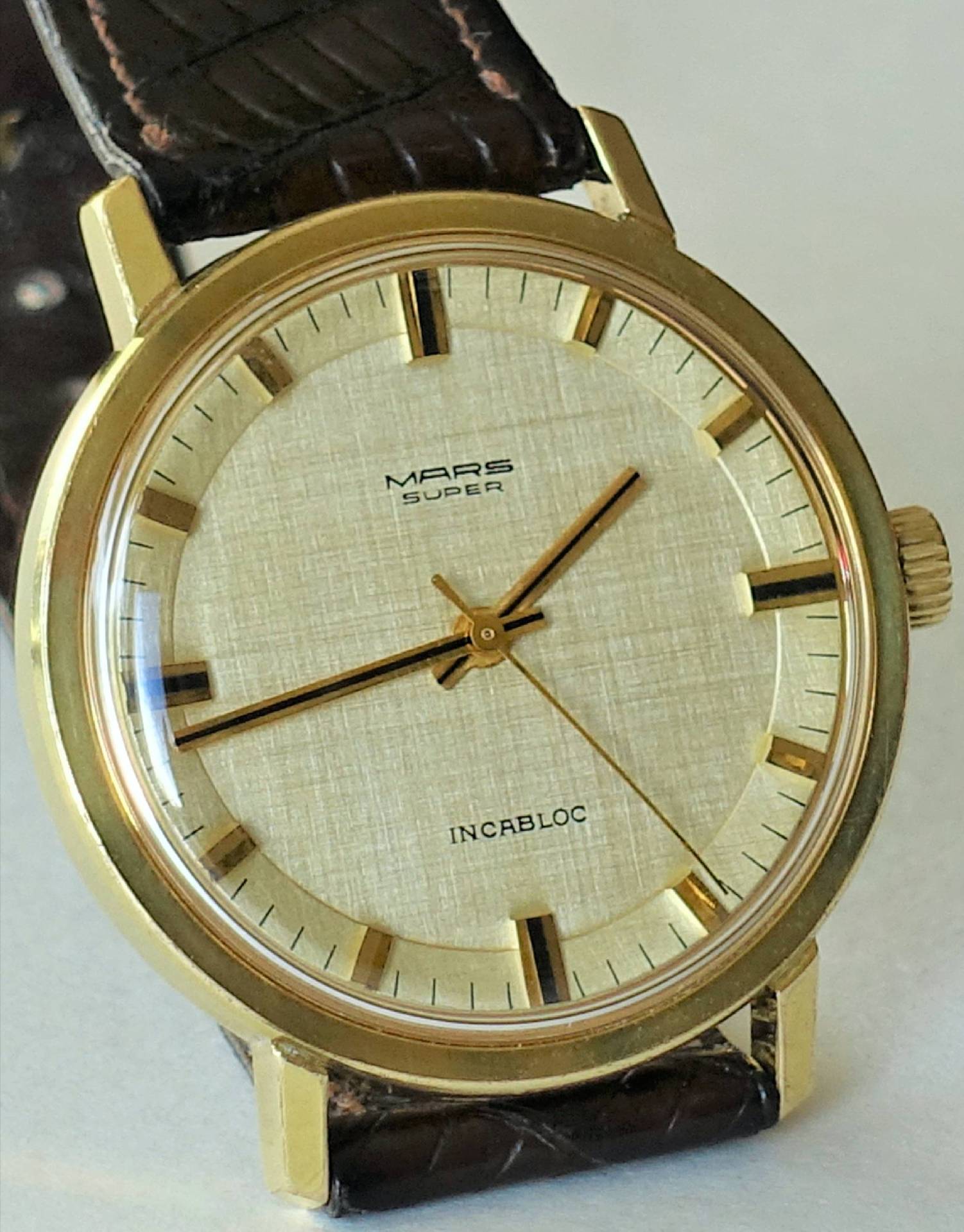 Goldfarbene Mars Super Armbanduhr mit hellem Zifferblatt und braunem Armband.