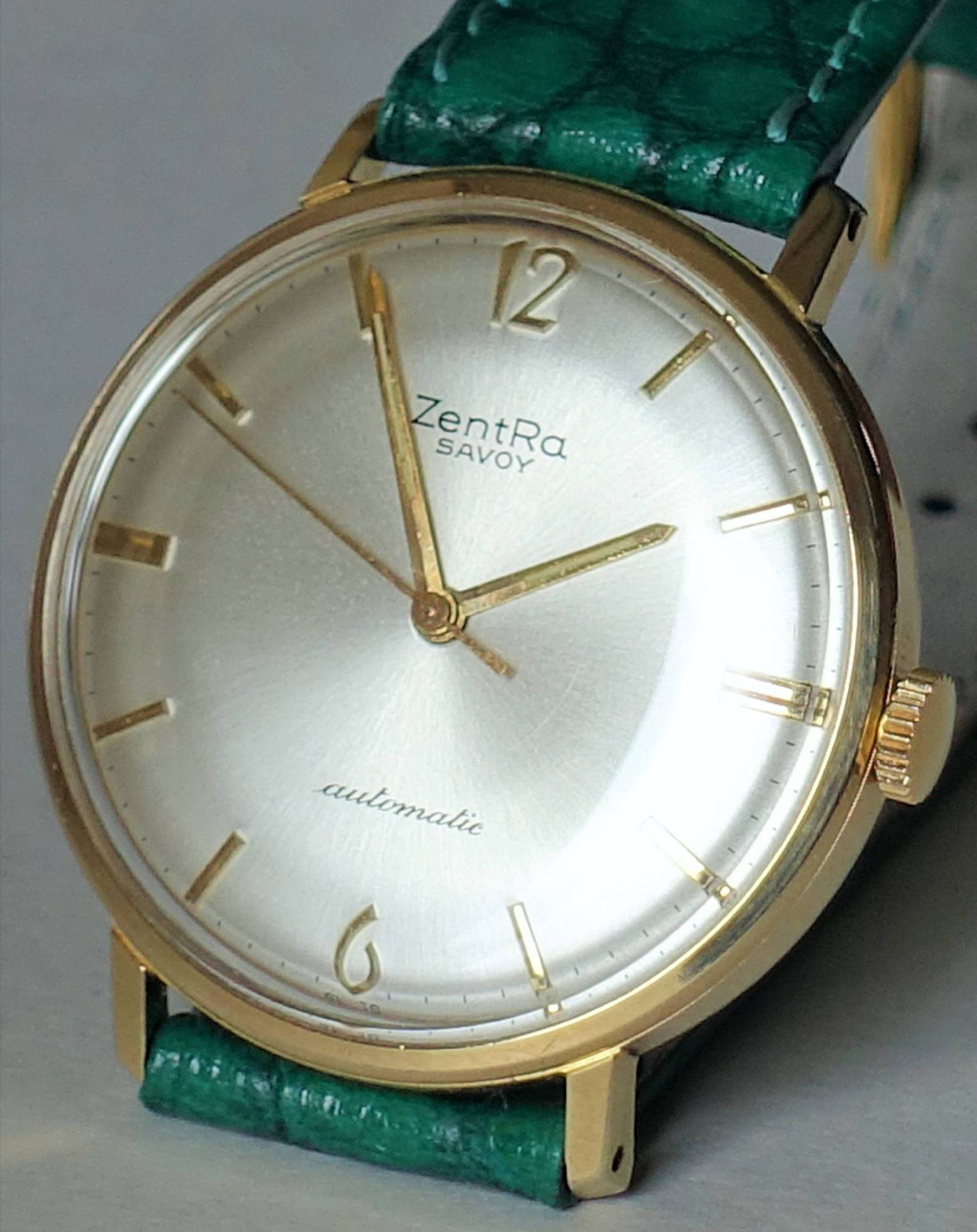Goldfarbene Armbanduhr mit hellem Zifferblatt und grünem Armband.