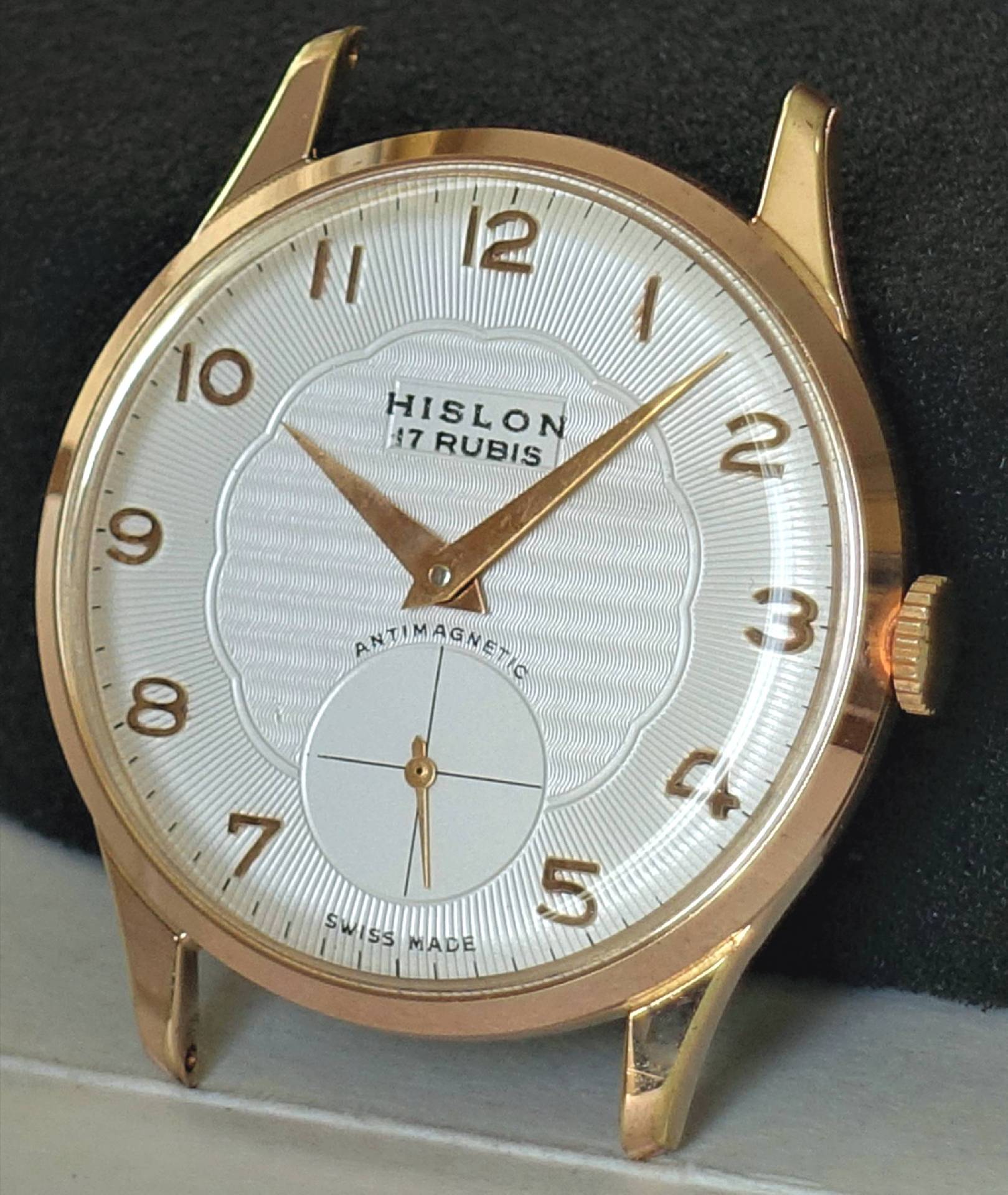 Eine klassische Armbanduhr mit weißem Zifferblatt, goldfarbenem Gehäuse und goldfarbenen Zeigern, sowie arabischen Ziffern und einer kleinen Sekunde bei sechs Uhr.