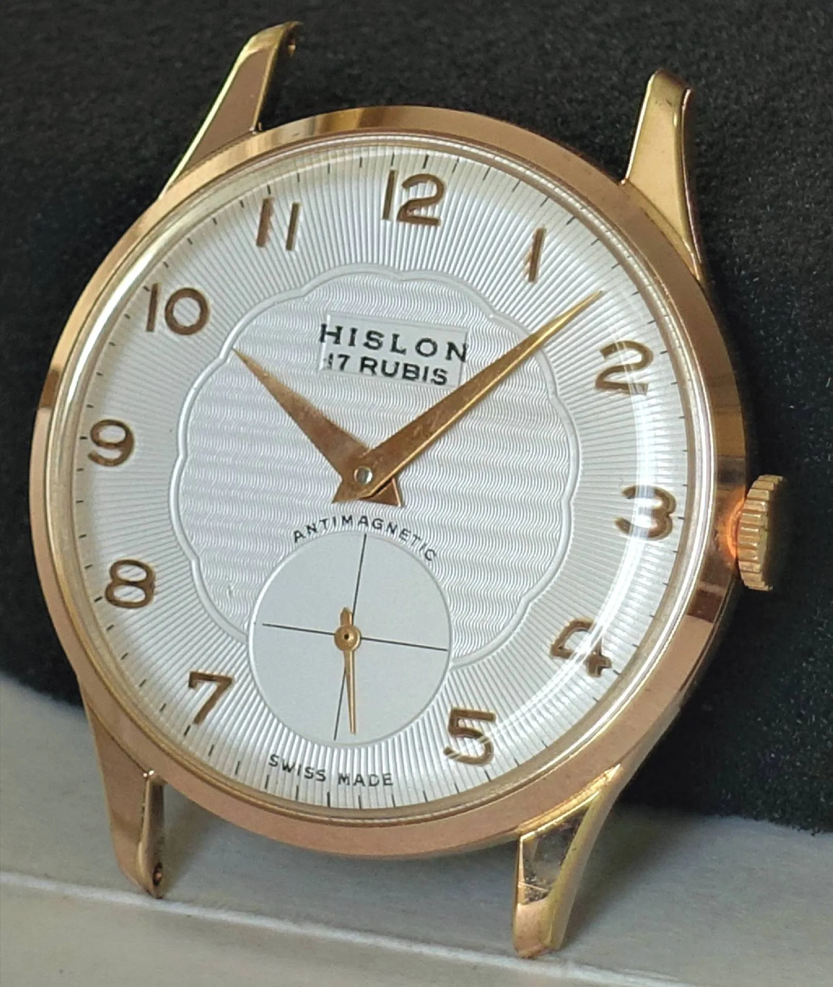 Eine klassische Armbanduhr mit weißem Zifferblatt, goldfarbenem Gehäuse und goldfarbenen Zeigern, sowie arabischen Ziffern und einer kleinen Sekunde bei sechs Uhr.