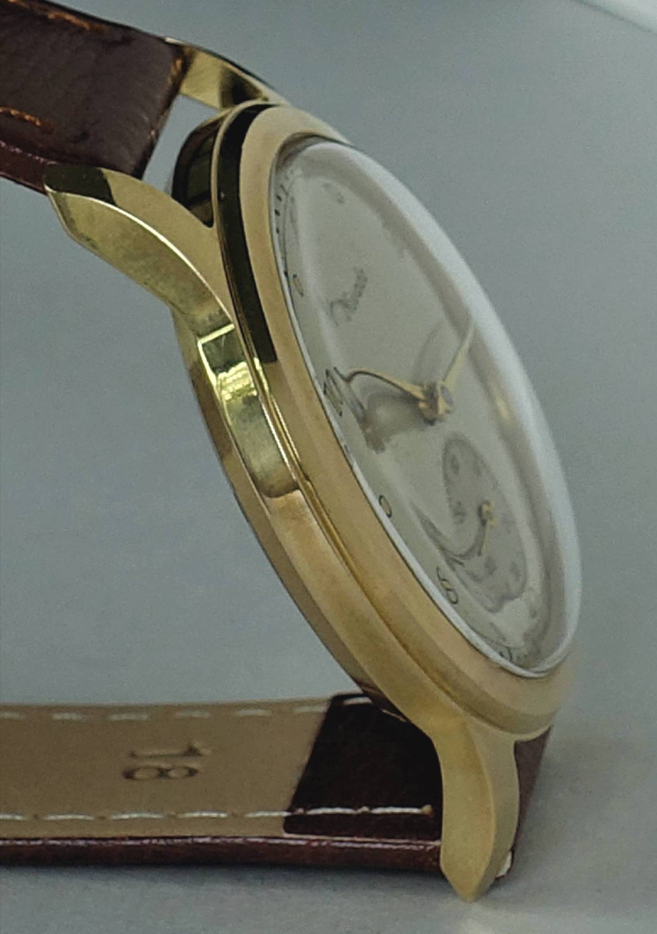 Goldfarbene Armbanduhr mit braunem Lederarmband und hellem Zifferblatt.