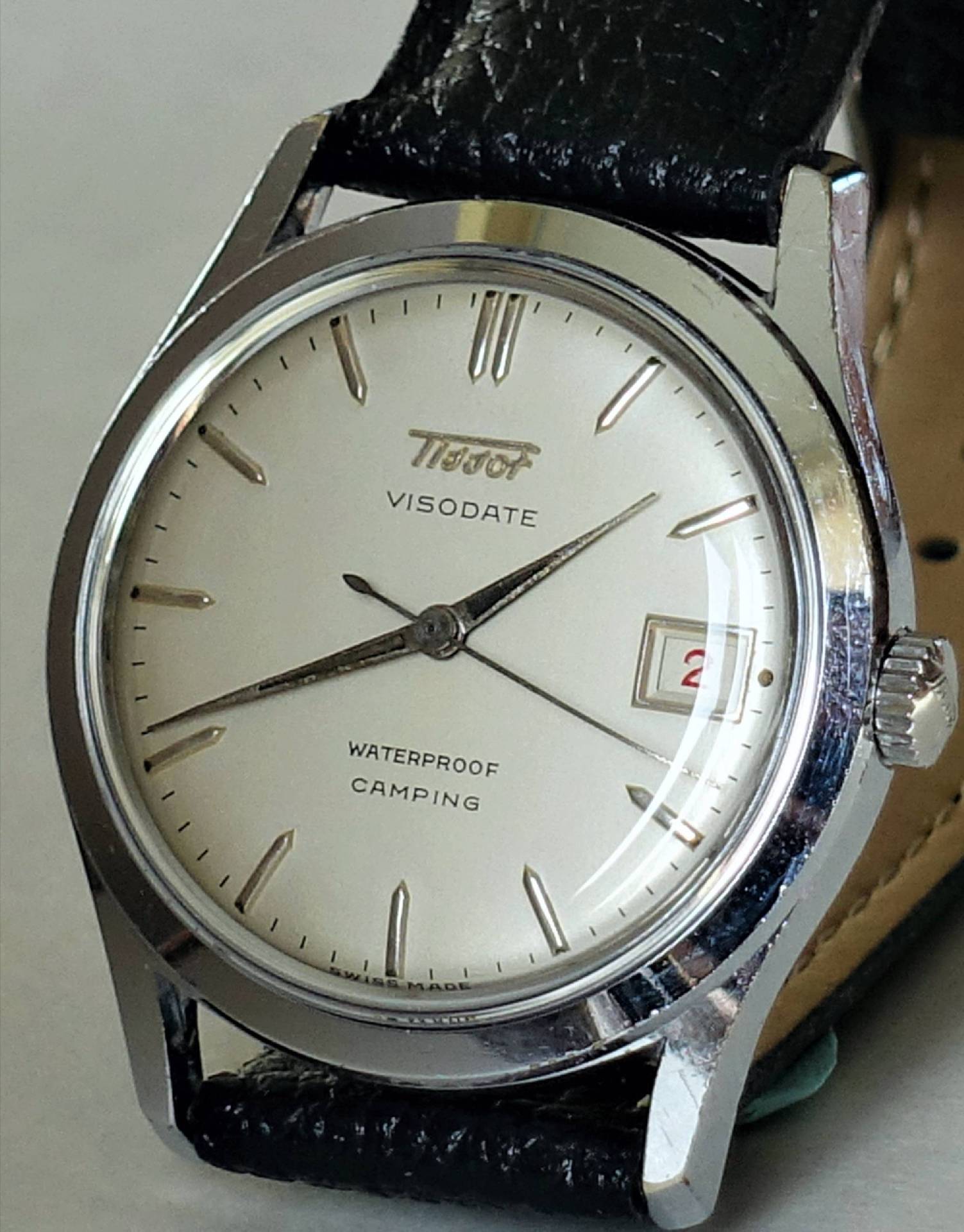 Silberfarbene Armbanduhr mit hellem Zifferblatt, schwarzem Lederarmband und Datumsanzeige.