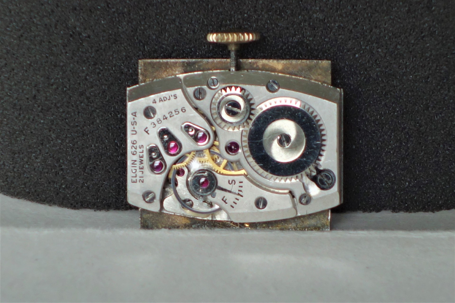 Silberfarbenes mechanisches Uhrwerk mit sichtbaren Zahnrädern und roten Lagersteinen.