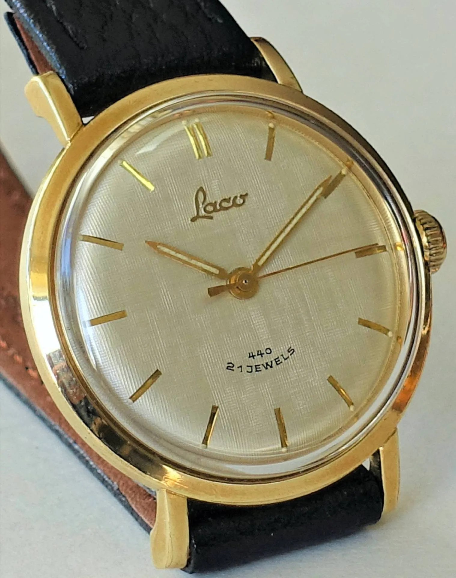 Analoge Armbanduhr mit goldfarbenem Gehäuse, hellem Zifferblatt und schwarzem Armband.