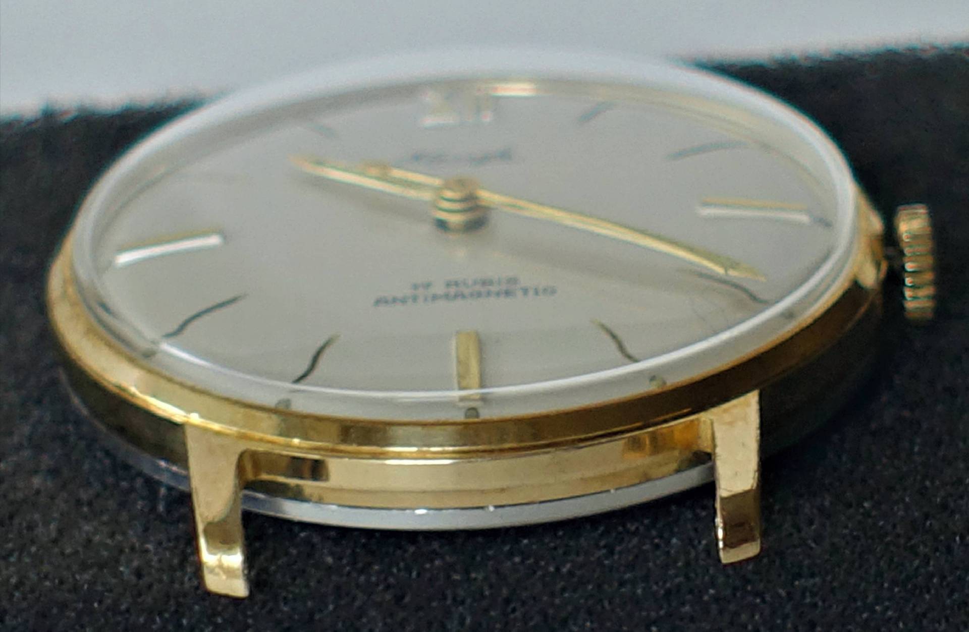 Flache Armbanduhr mit goldfarbenem Gehäuse und hellem Zifferblatt.