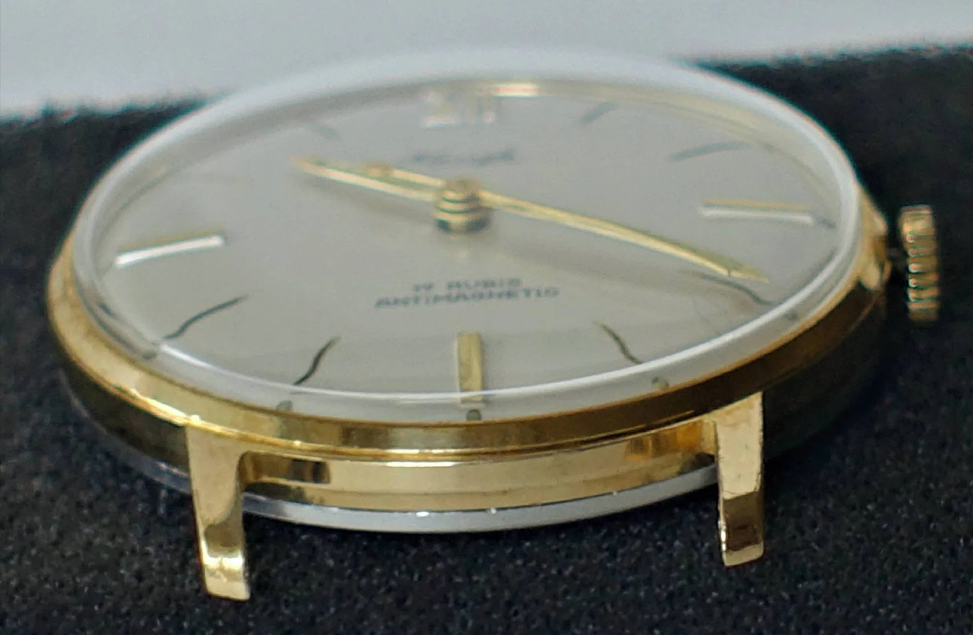 Flache Armbanduhr mit goldfarbenem Gehäuse und hellem Zifferblatt.