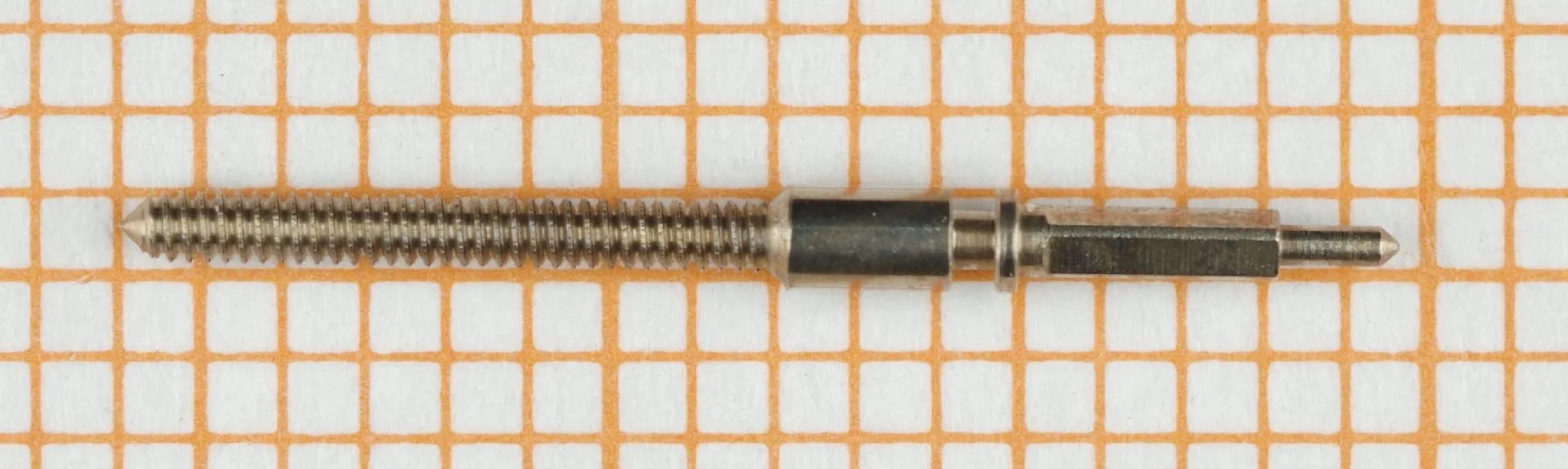 Metallene Aufzugswelle für Armbanduhren, liegend auf Millimeterpapier.