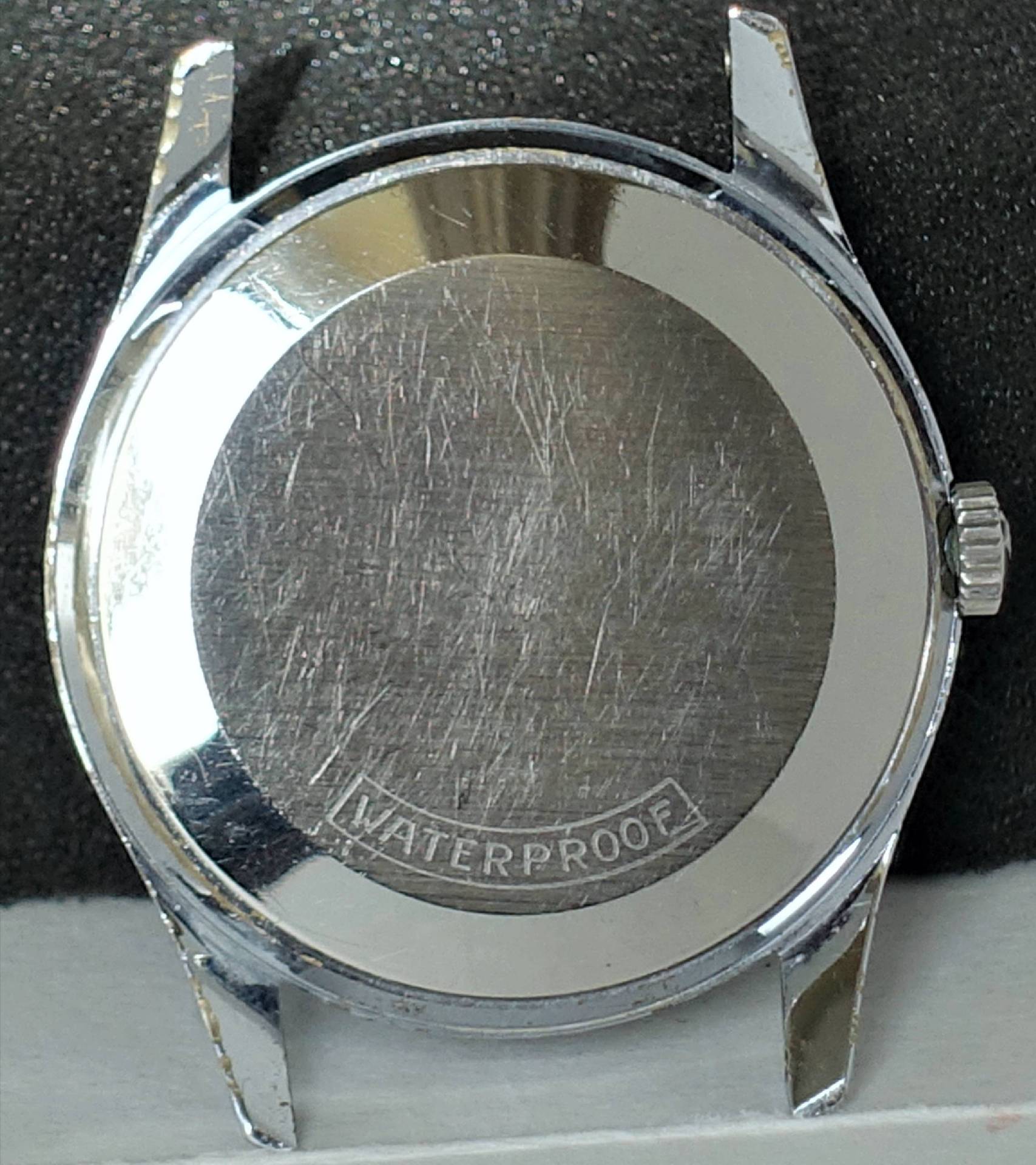 Silberfarbenes Uhrgehäuse mit verschraubtem Boden und seitlicher Krone.