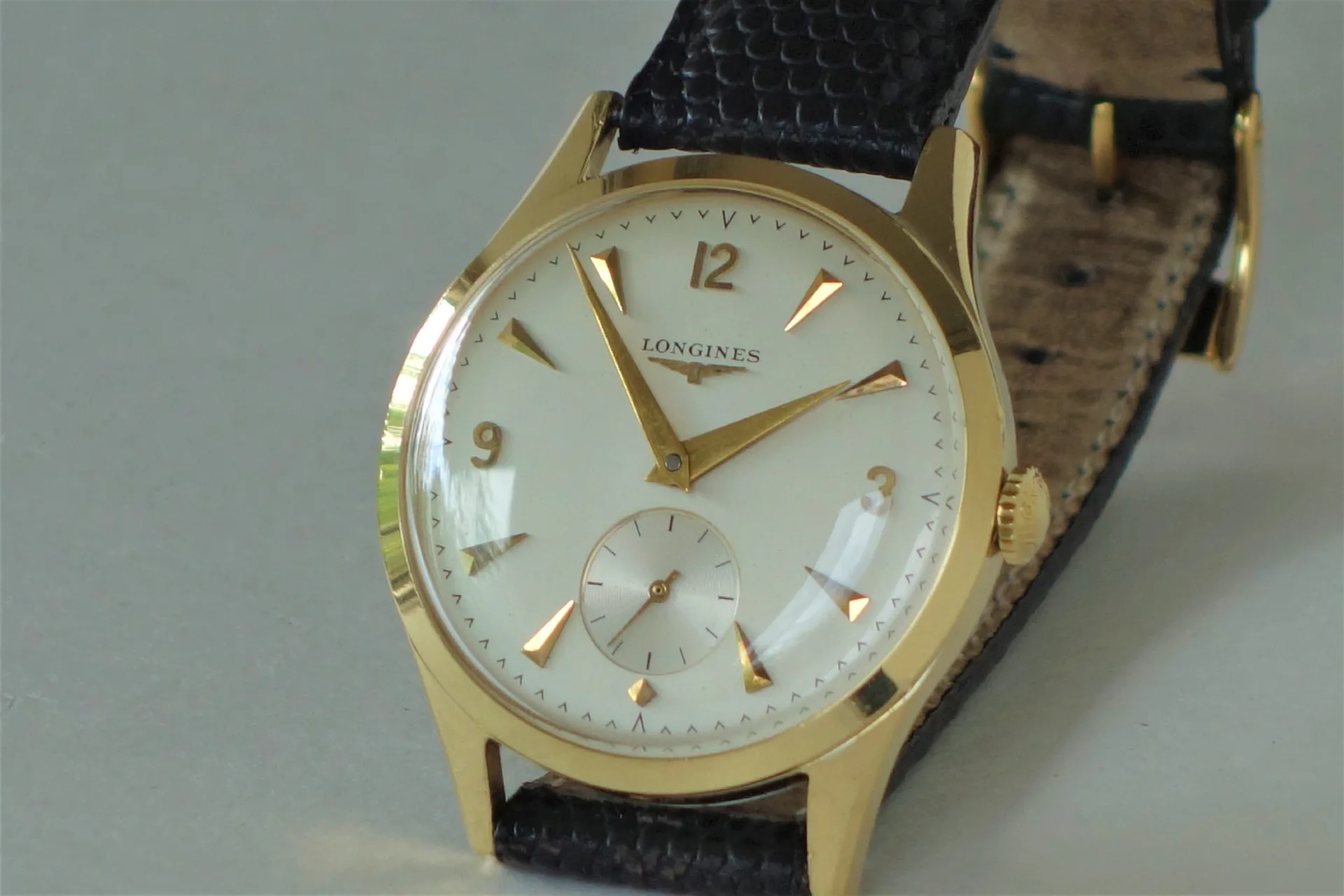 Klassische Armbanduhr mit goldfarbenem Gehäuse, weißem Zifferblatt und schwarzem Armband.