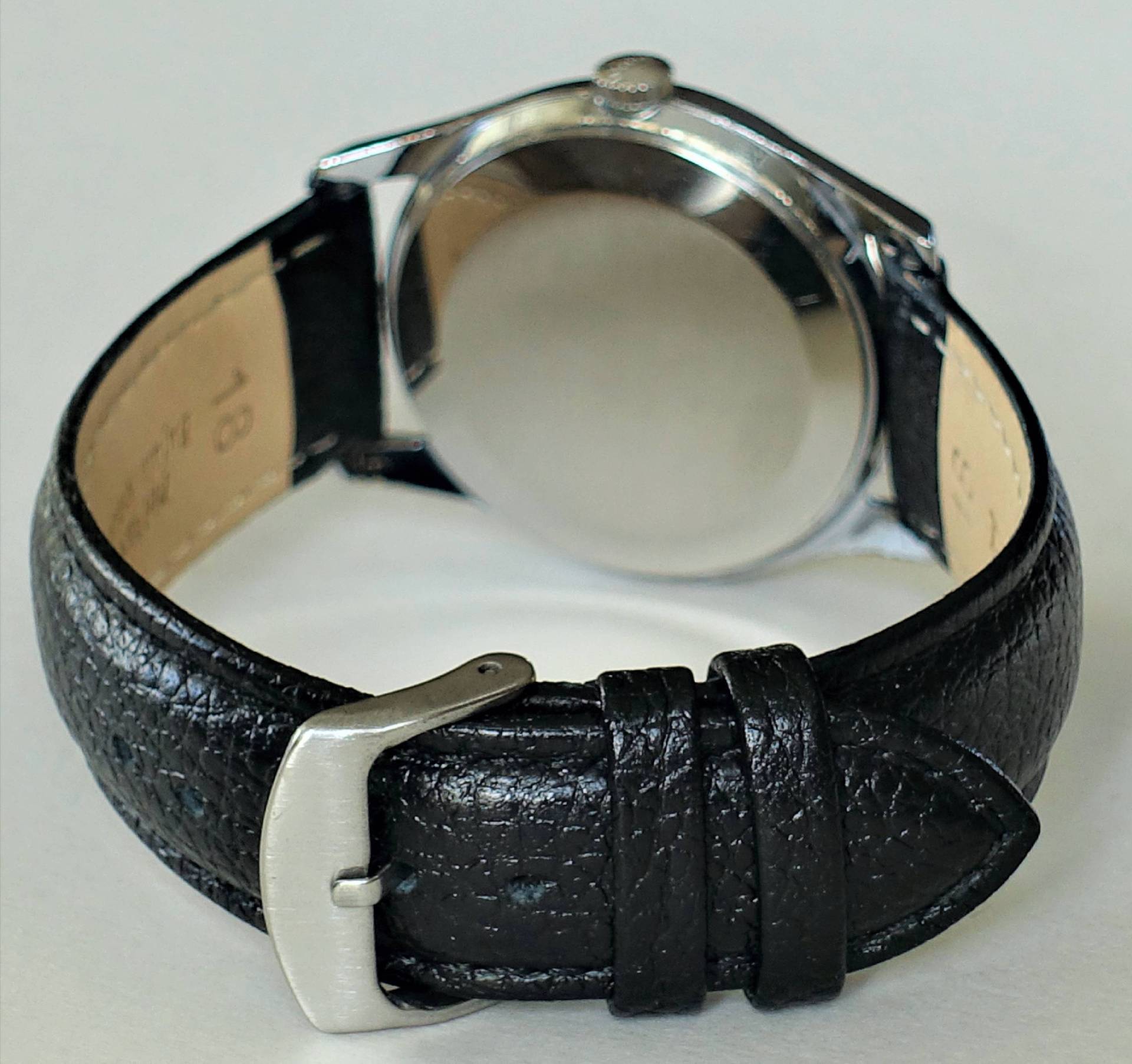 Schwarze Armbanduhr mit rundem silberfarbenem Gehäuse und schwarzem Lederarmband.