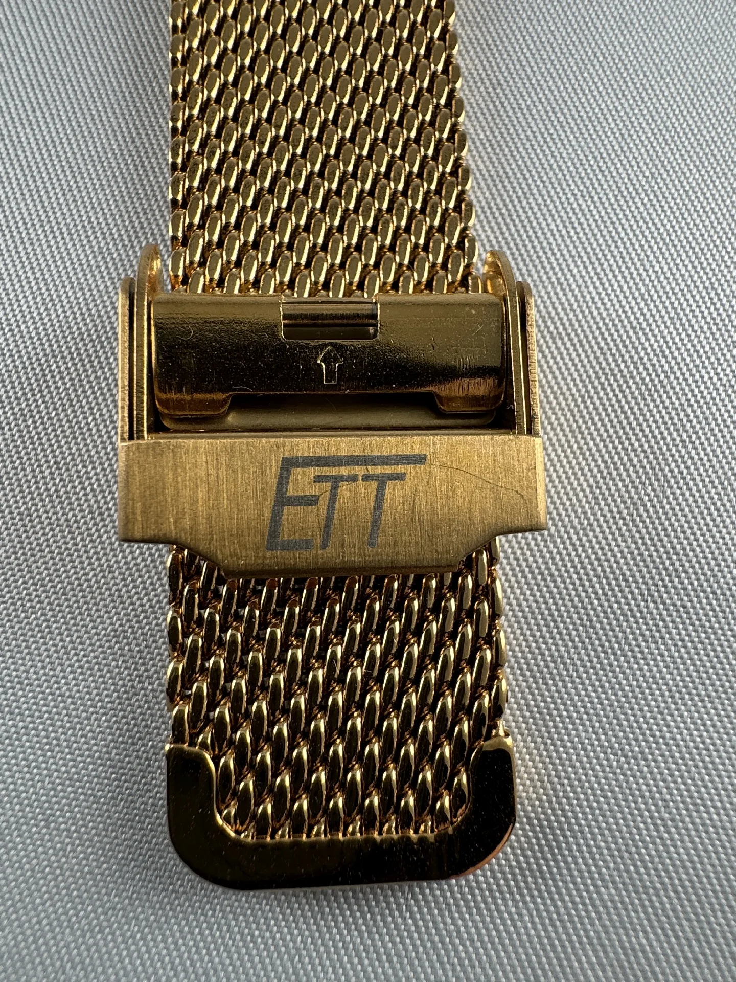 Milanaise Armband goldfarben Goldfarbenes Milanaise-Uhrenarmband mit Faltschließe und ETT-Logo.