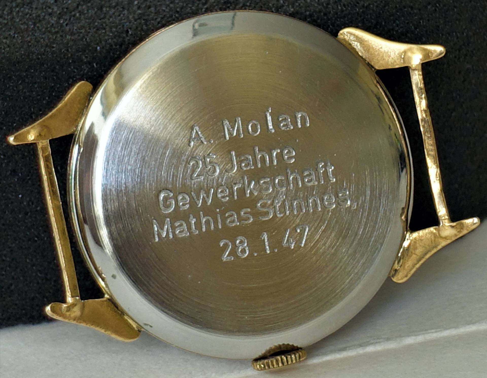 Silberfarbener Uhrboden mit Gravur und goldfarbenen Bandanstößen.