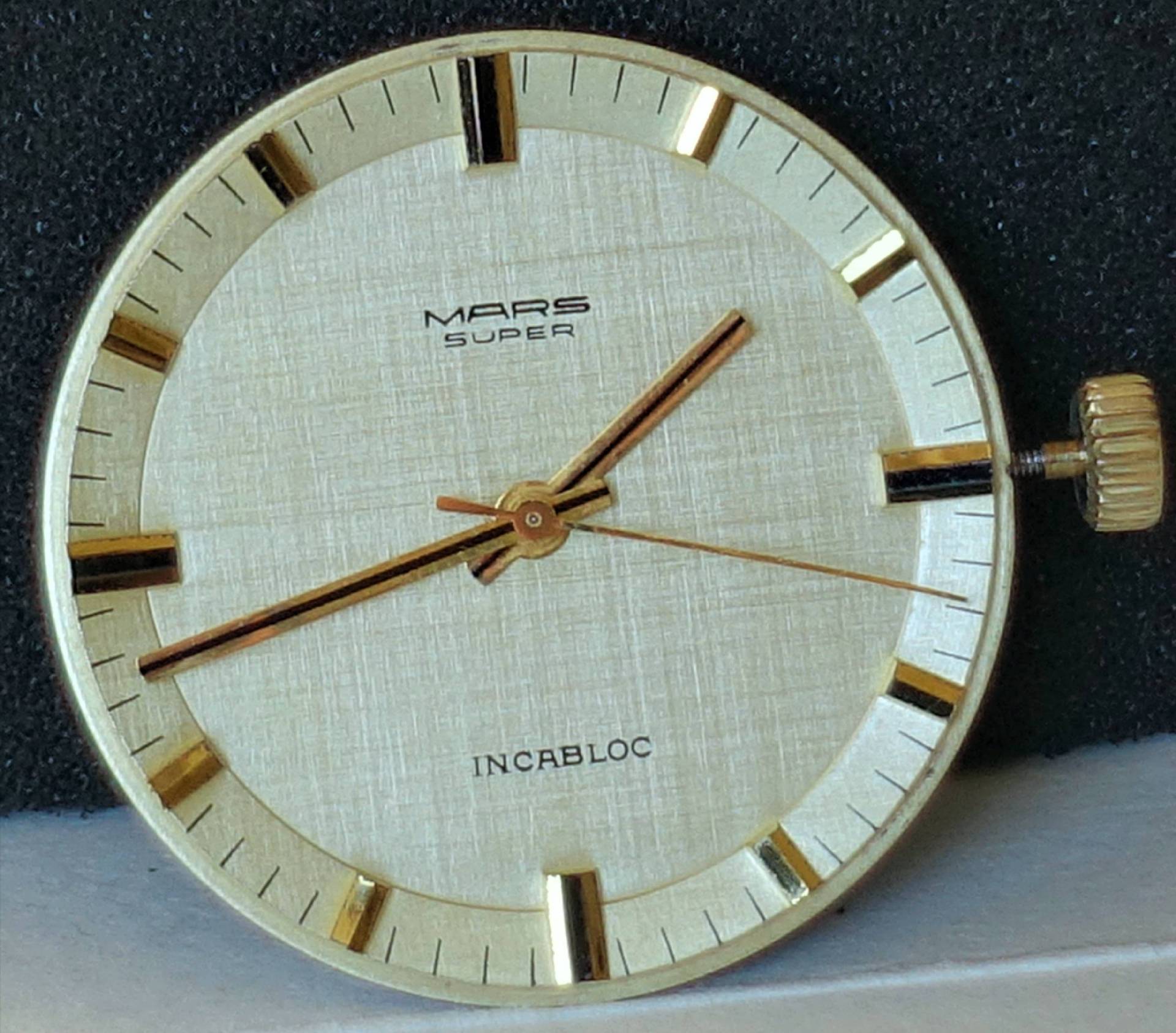 Rundes helles Uhrwerk mit goldfarbenen Zeigern und Zifferblatt, Aufschrift "MARS SUPER" und "INCABLOC".