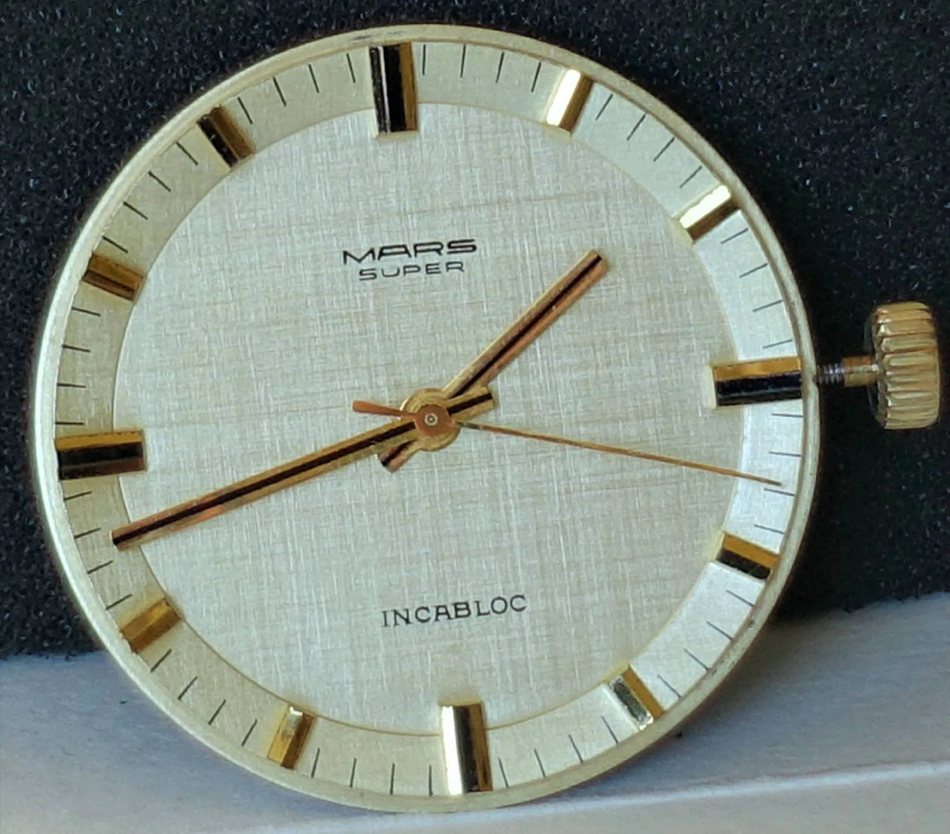 Rundes helles Uhrwerk mit goldfarbenen Zeigern und Zifferblatt, Aufschrift "MARS SUPER" und "INCABLOC".