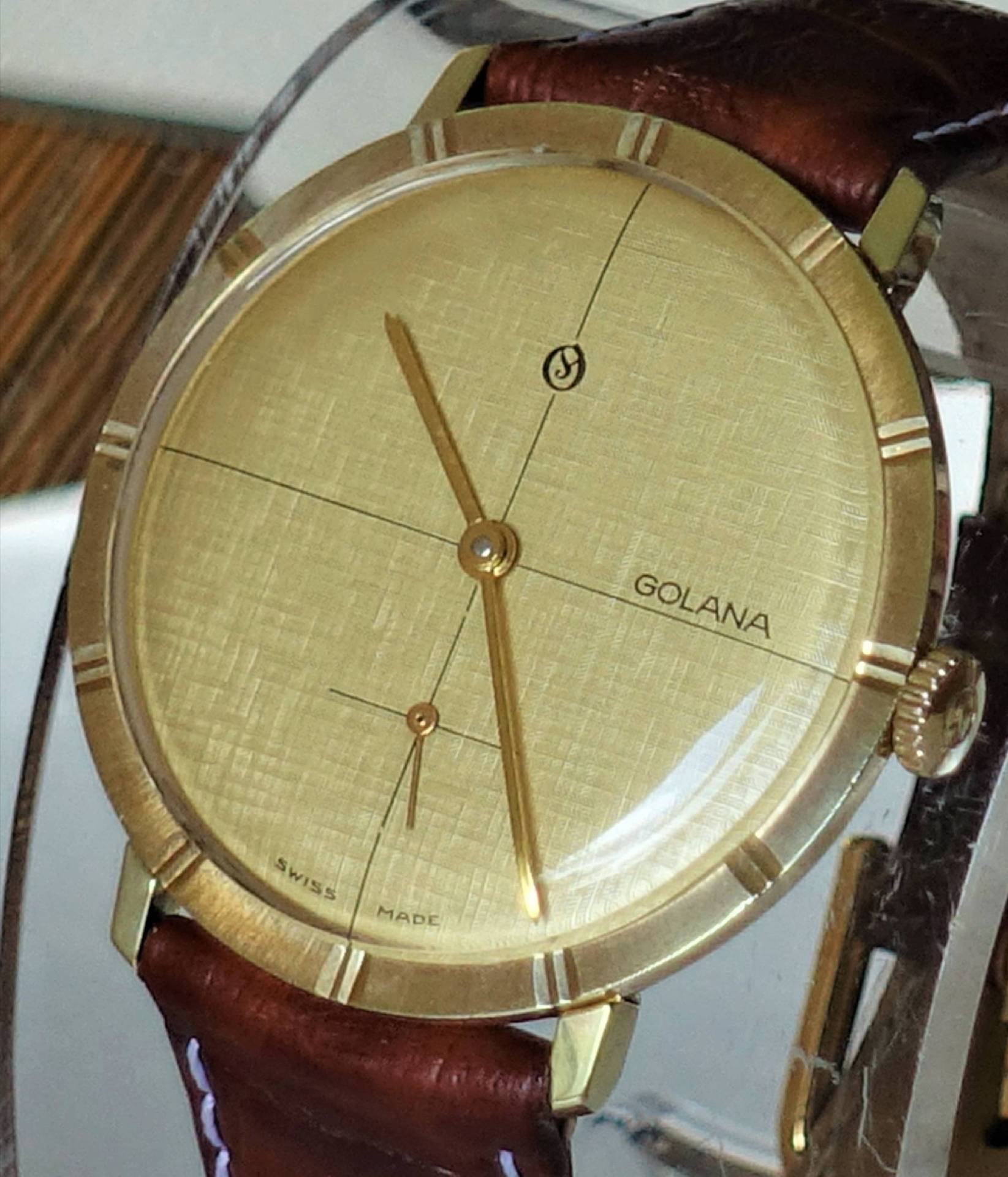 Goldfarbene Armbanduhr mit braunem Lederarmband und schlichtem Zifferblatt.
