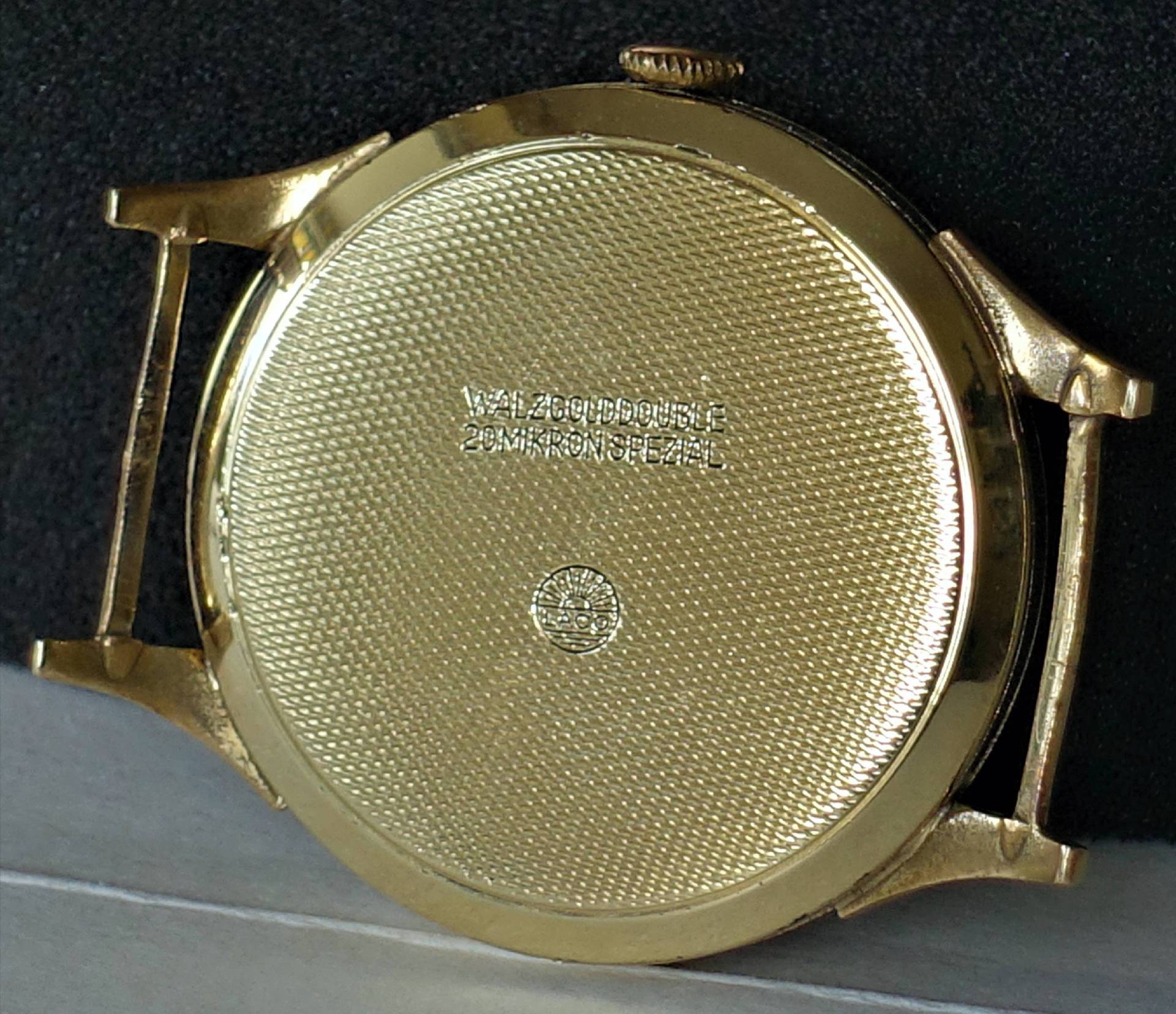 Rückseite eines goldfarbenen Uhrengehäuses mit feiner Struktur und Gravur.