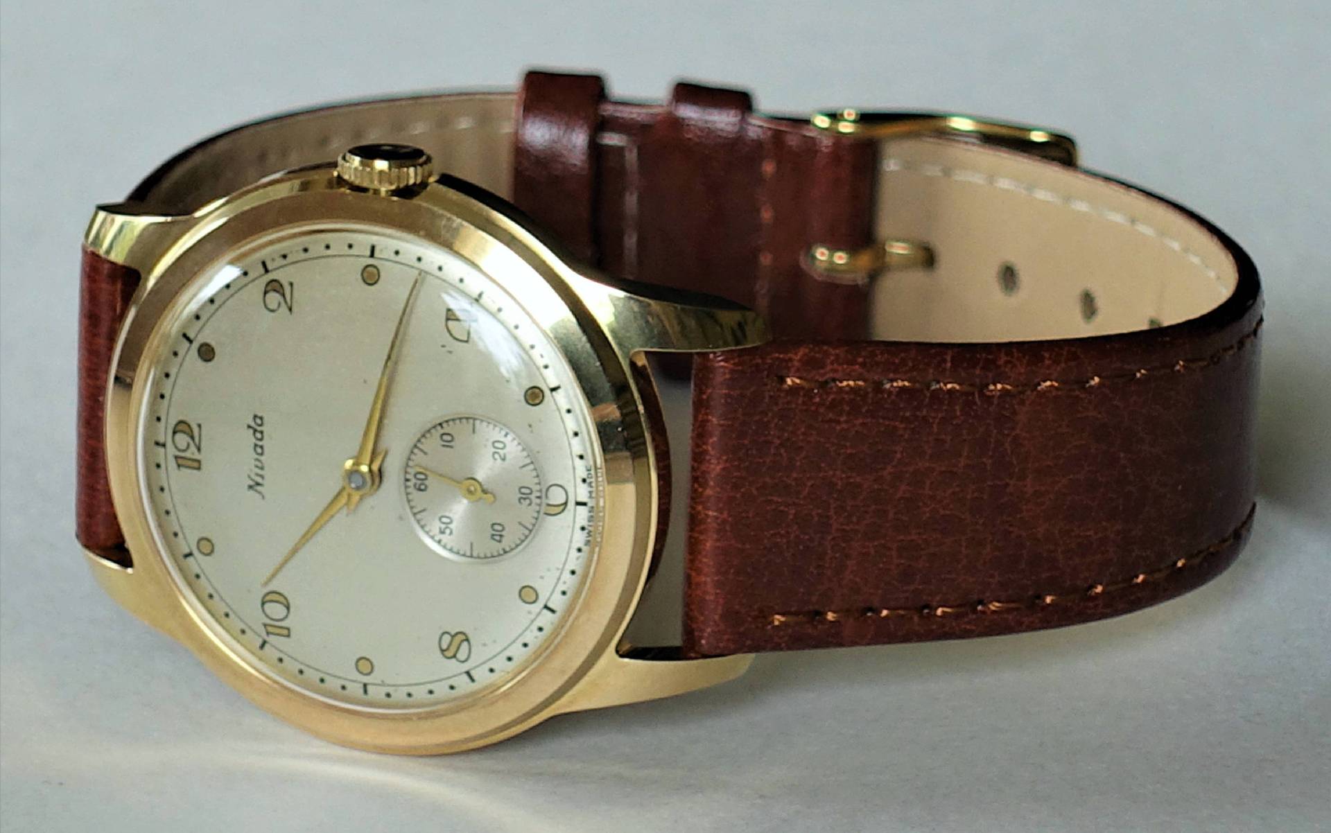 Goldfarbene Armbanduhr mit braunem Lederarmband und hellem Zifferblatt.