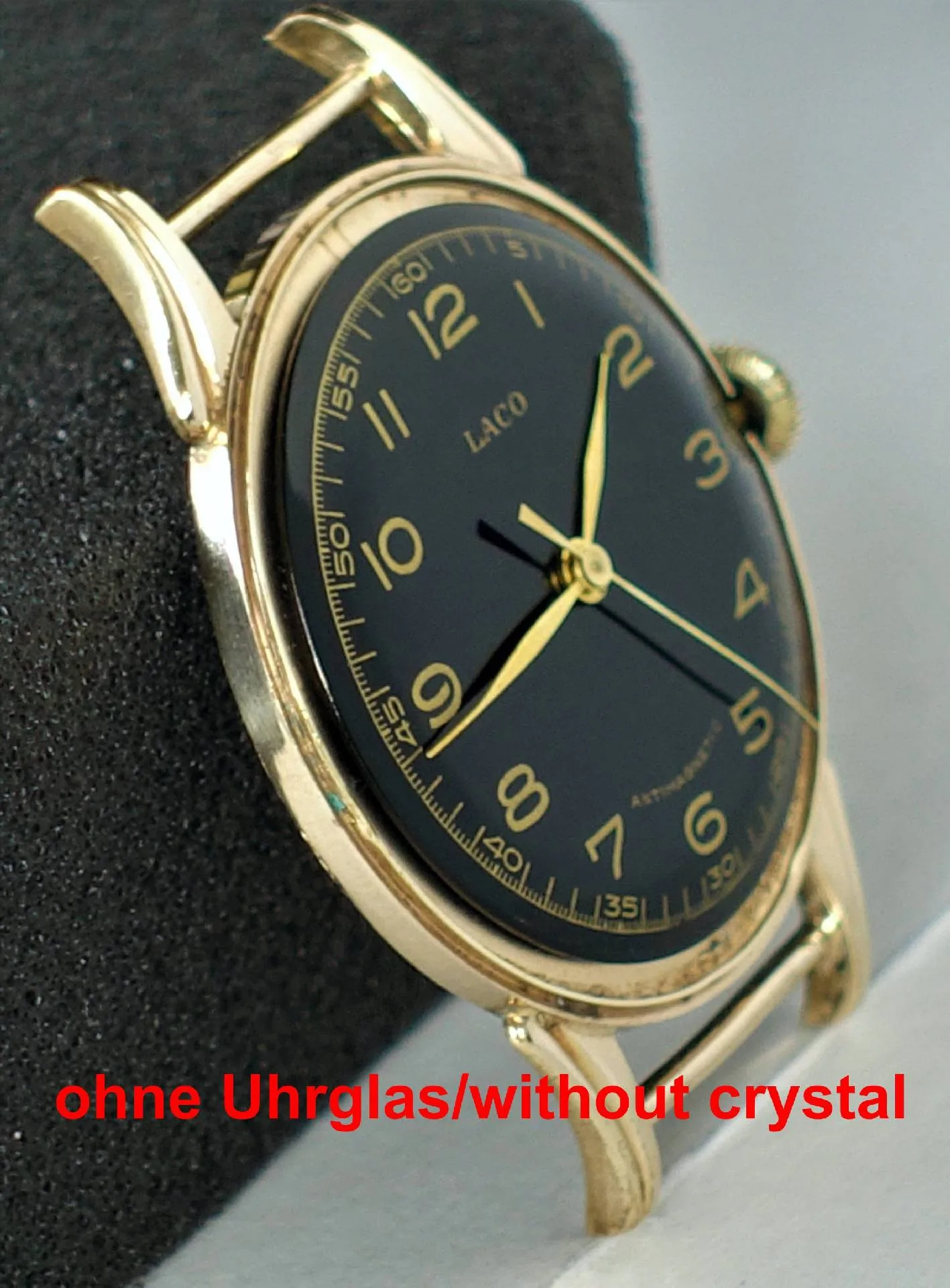Eine Armbanduhr mit schwarzem Zifferblatt und gelbem Gehäuse, ohne Uhrglas, liegt auf einem schwarzen Schaumstoffblock.
