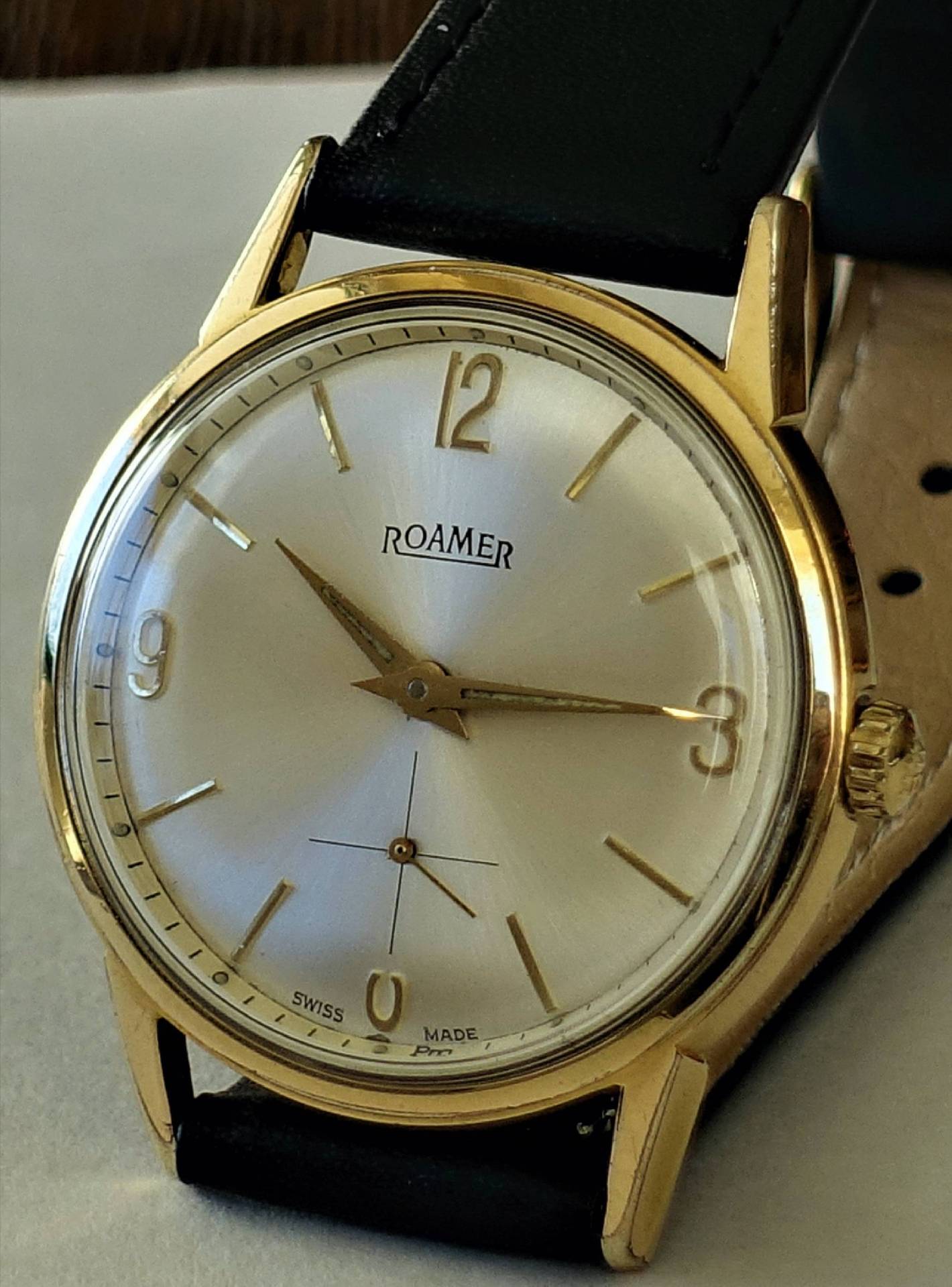 Goldfarbene Armbanduhr mit silbernem Zifferblatt und schwarzem Armband.