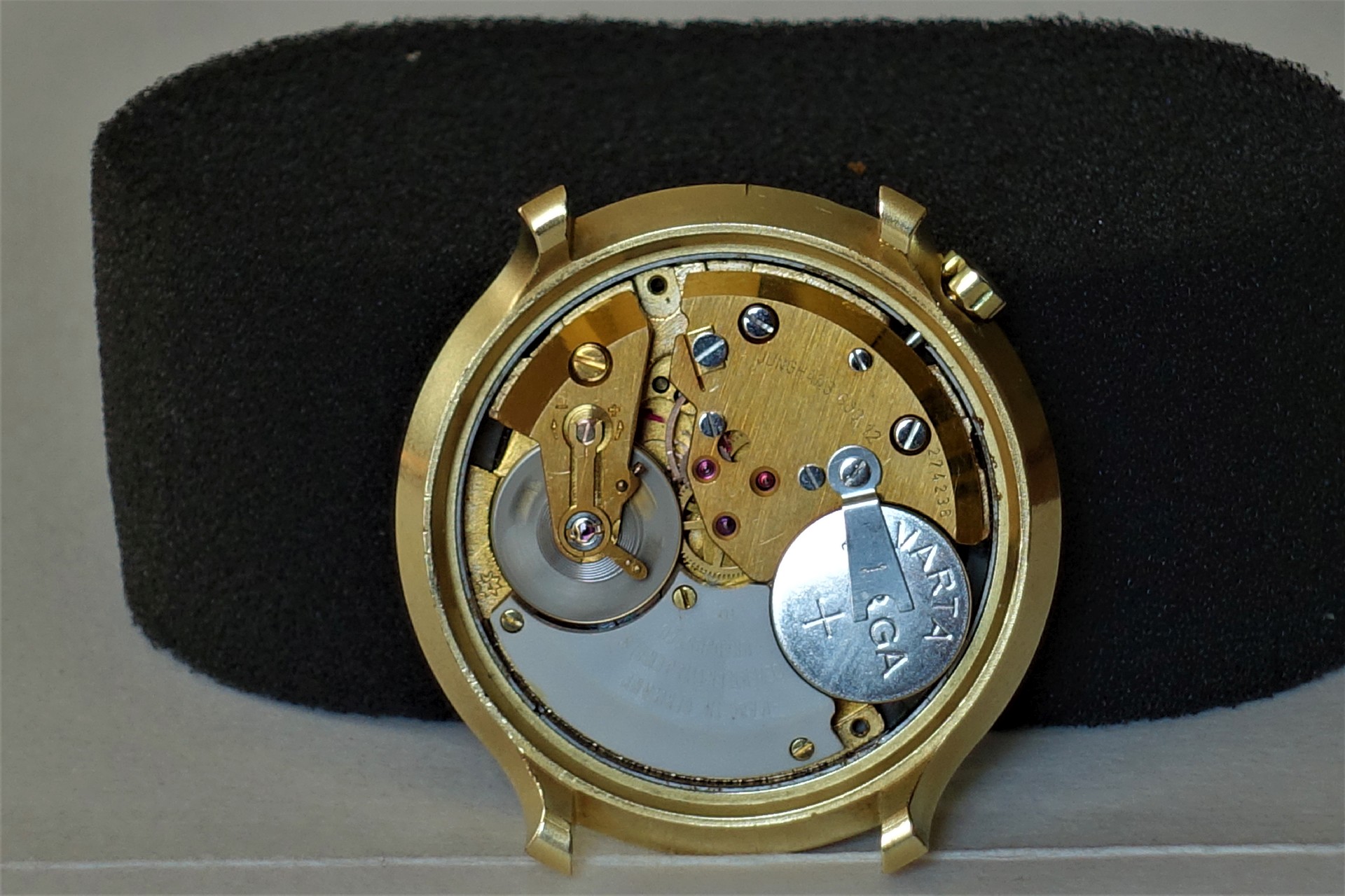 Geöffnetes goldfarbenes Quarzuhrwerk mit sichtbarer Batterie in einem Uhrengehäuse.