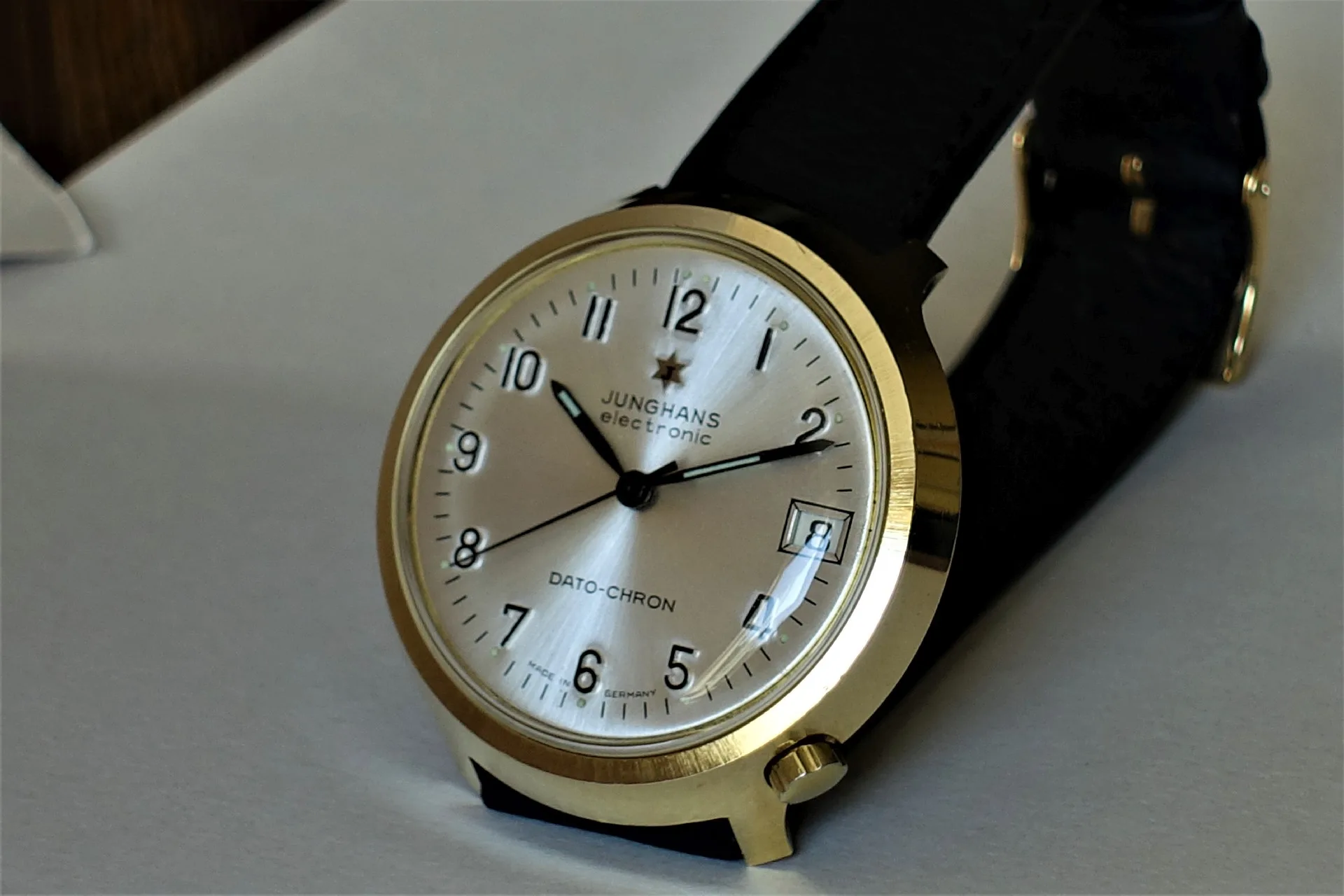 Junghans Armbanduhr goldfarben Analoge Armbanduhr mit goldfarbenem Gehäuse, hellem Zifferblatt und schwarzem Armband.