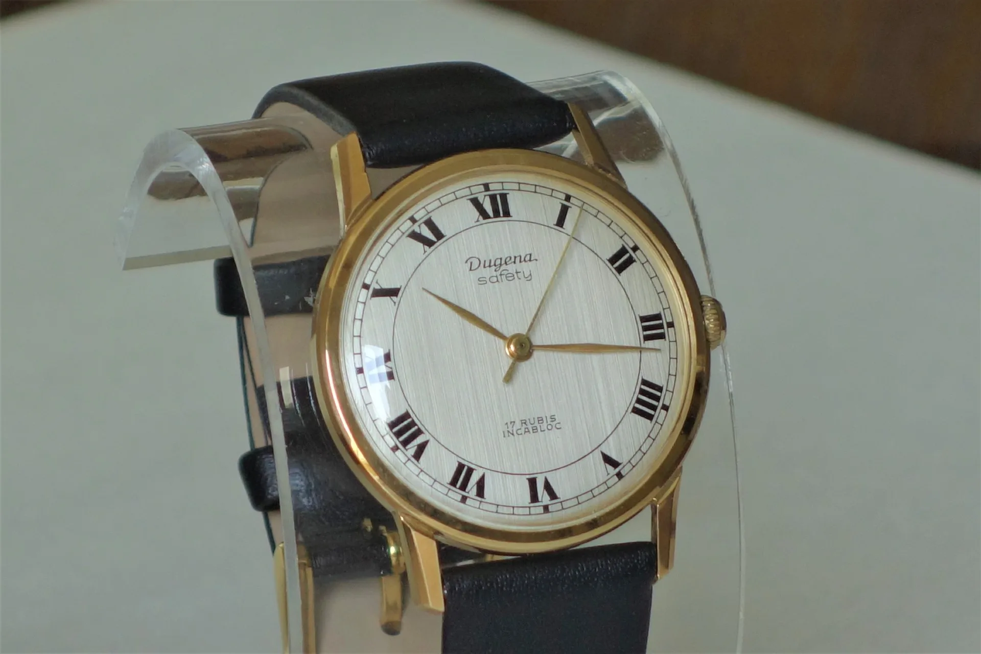 Klassische Armbanduhr mit goldfarbenem Gehäuse, hellem Zifferblatt und schwarzem Lederarmband.
