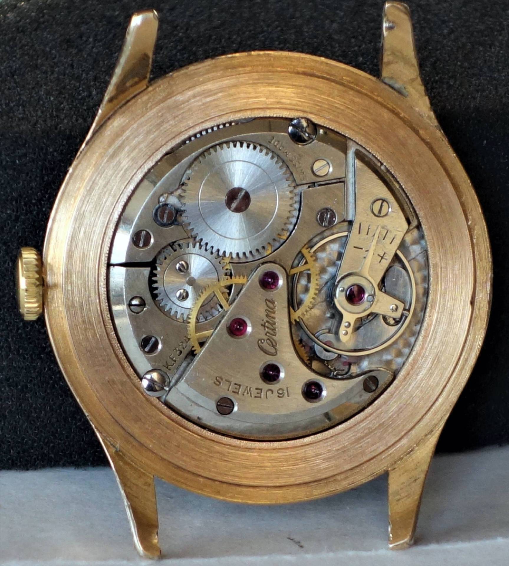 Mechanisches Uhrwerk in einem goldfarbenen Gehäuse mit sichtbaren Zahnrädern und Schrauben.