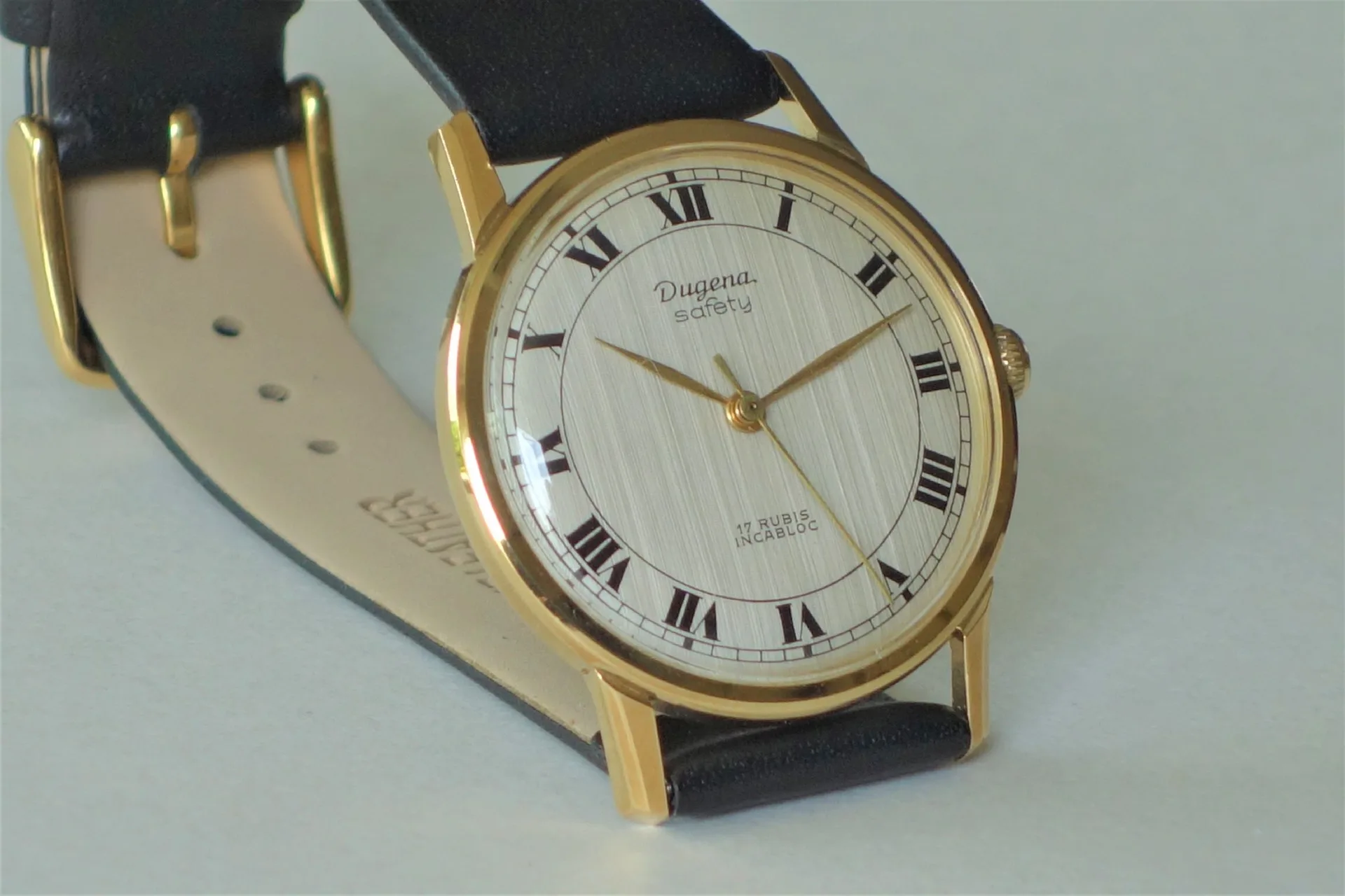 Runde Armbanduhr mit goldfarbenem Gehäuse, hellem Zifferblatt mit römischen Zahlen und schwarzem Armband.