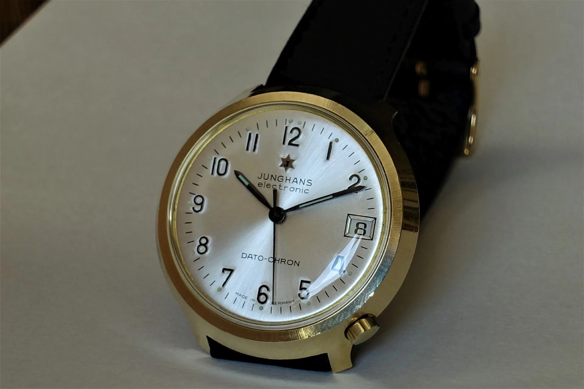 Junghans Armbanduhr goldfarben Analoge Armbanduhr mit goldfarbenem Gehäuse, weißem Zifferblatt und schwarzem Lederarmband.