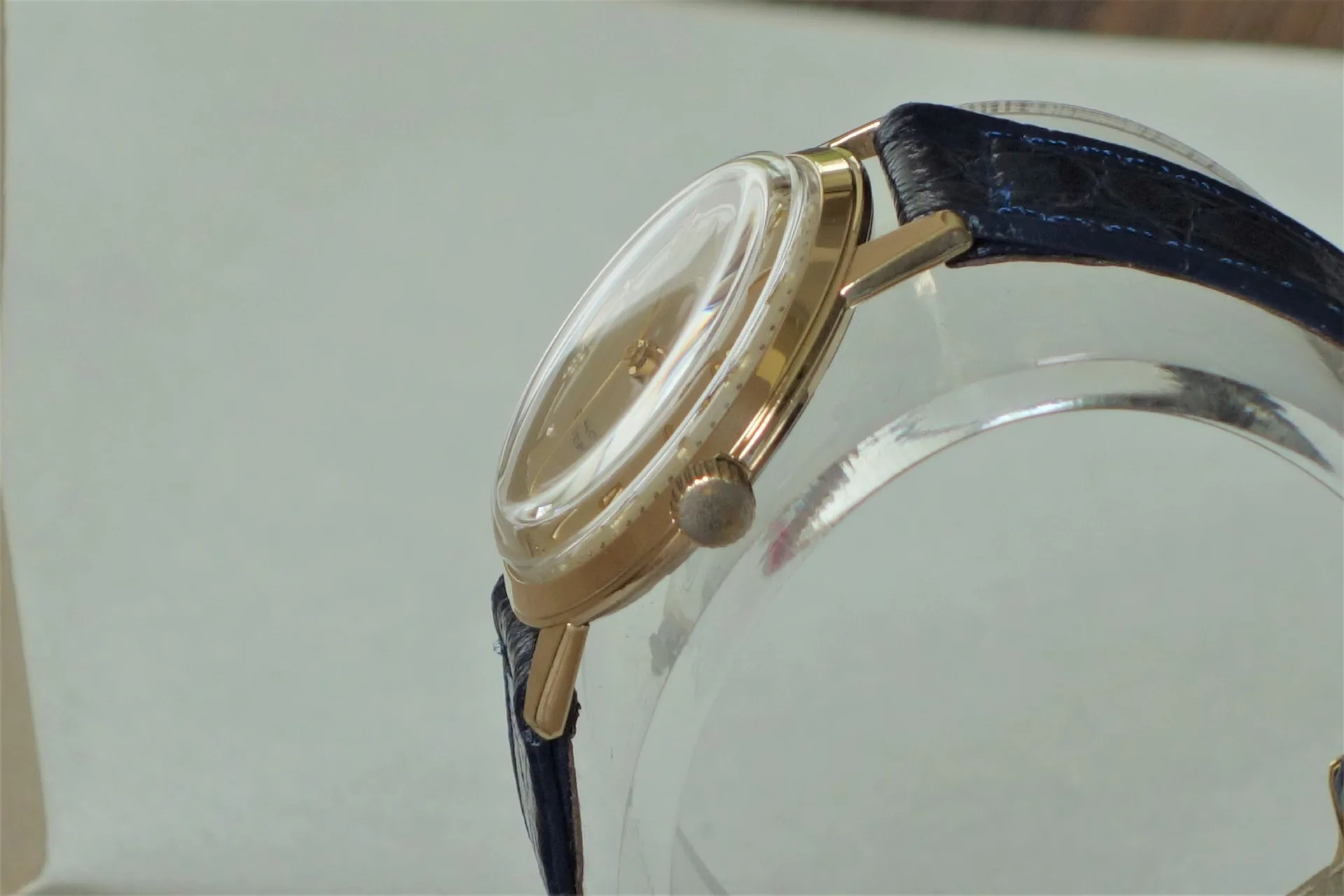 Goldfarbene Armbanduhr mit dunkelblauem Armband und gewölbtem Glas.
