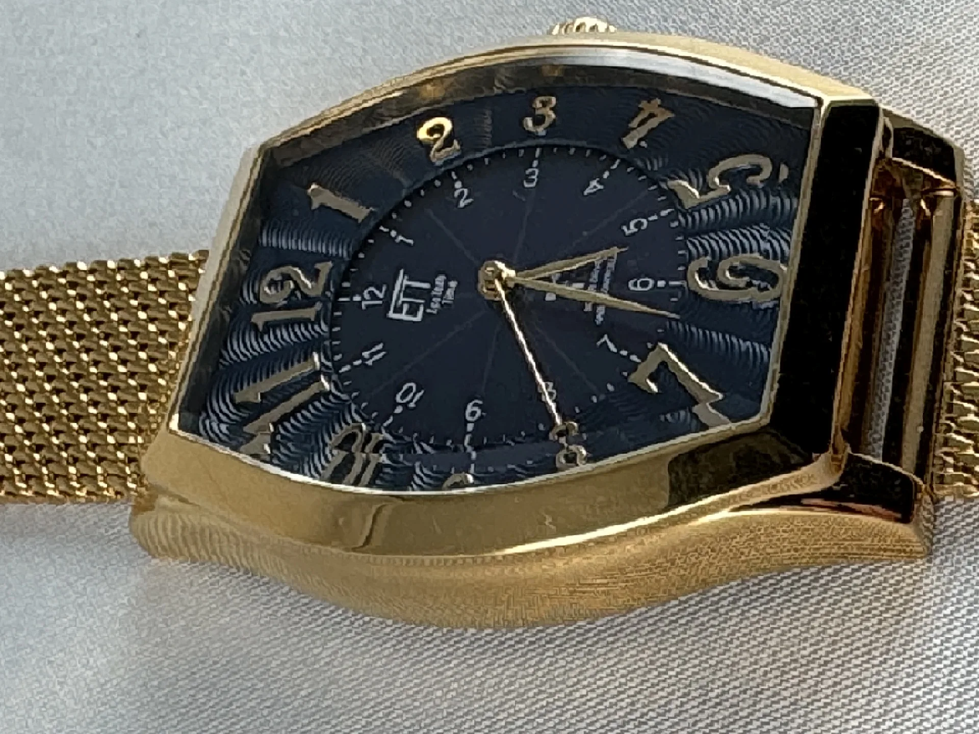 Goldfarbene Armbanduhr mit tonneauförmigem Gehäuse, schwarzem Zifferblatt und goldfarbenem Milanaise-Armband.