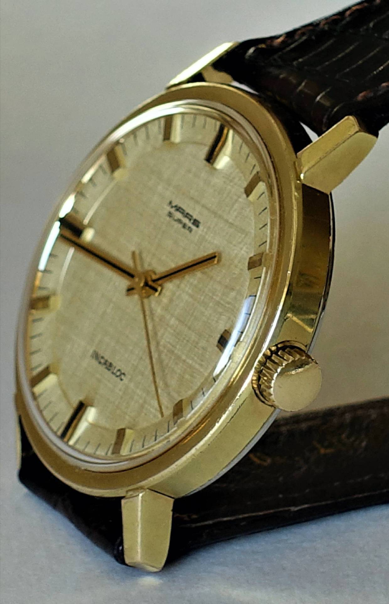 Goldfarbene Armbanduhr mit hellem Zifferblatt und dunklem Armband.