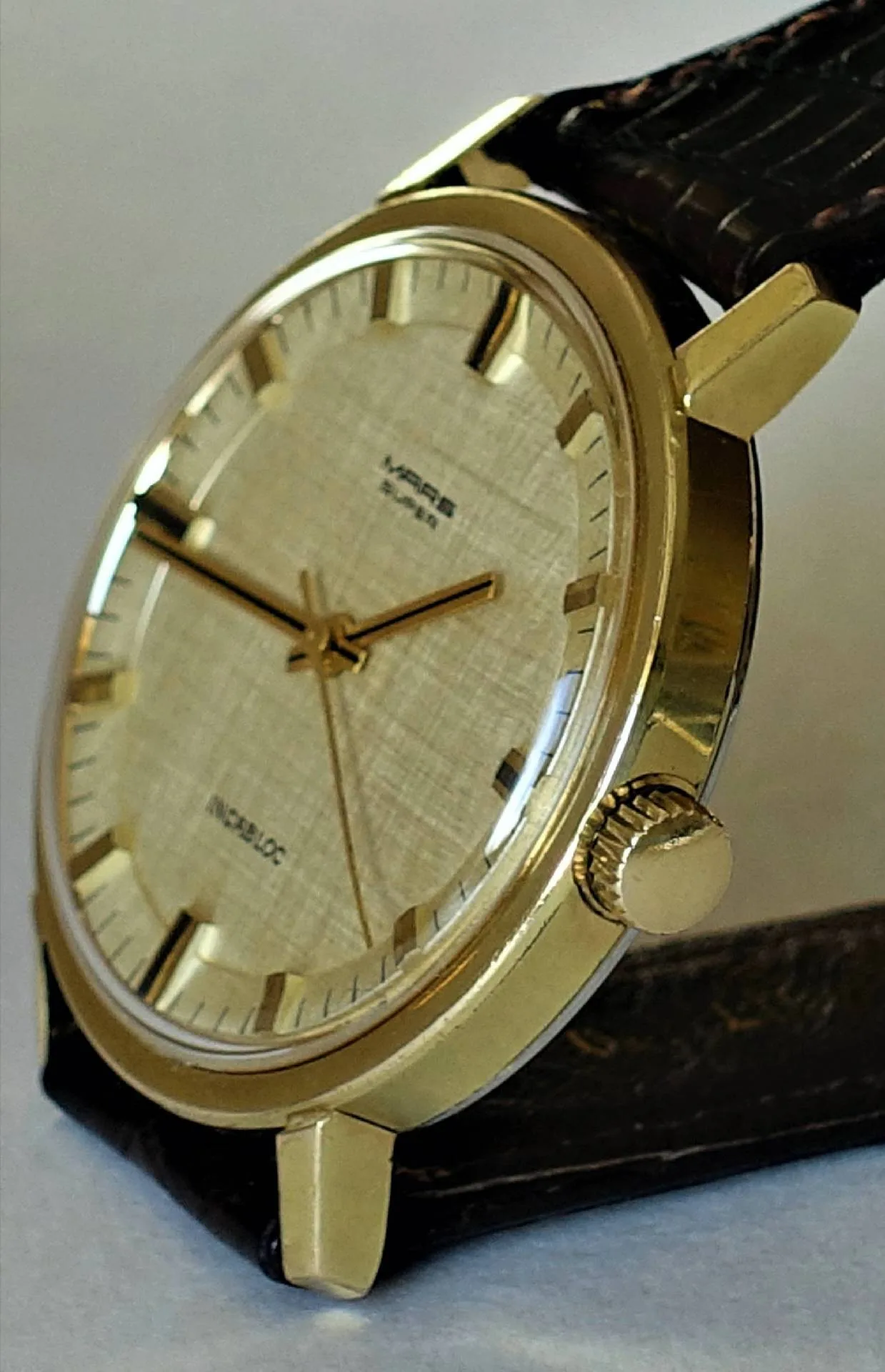 Goldfarbene Armbanduhr mit hellem Zifferblatt und dunklem Armband.