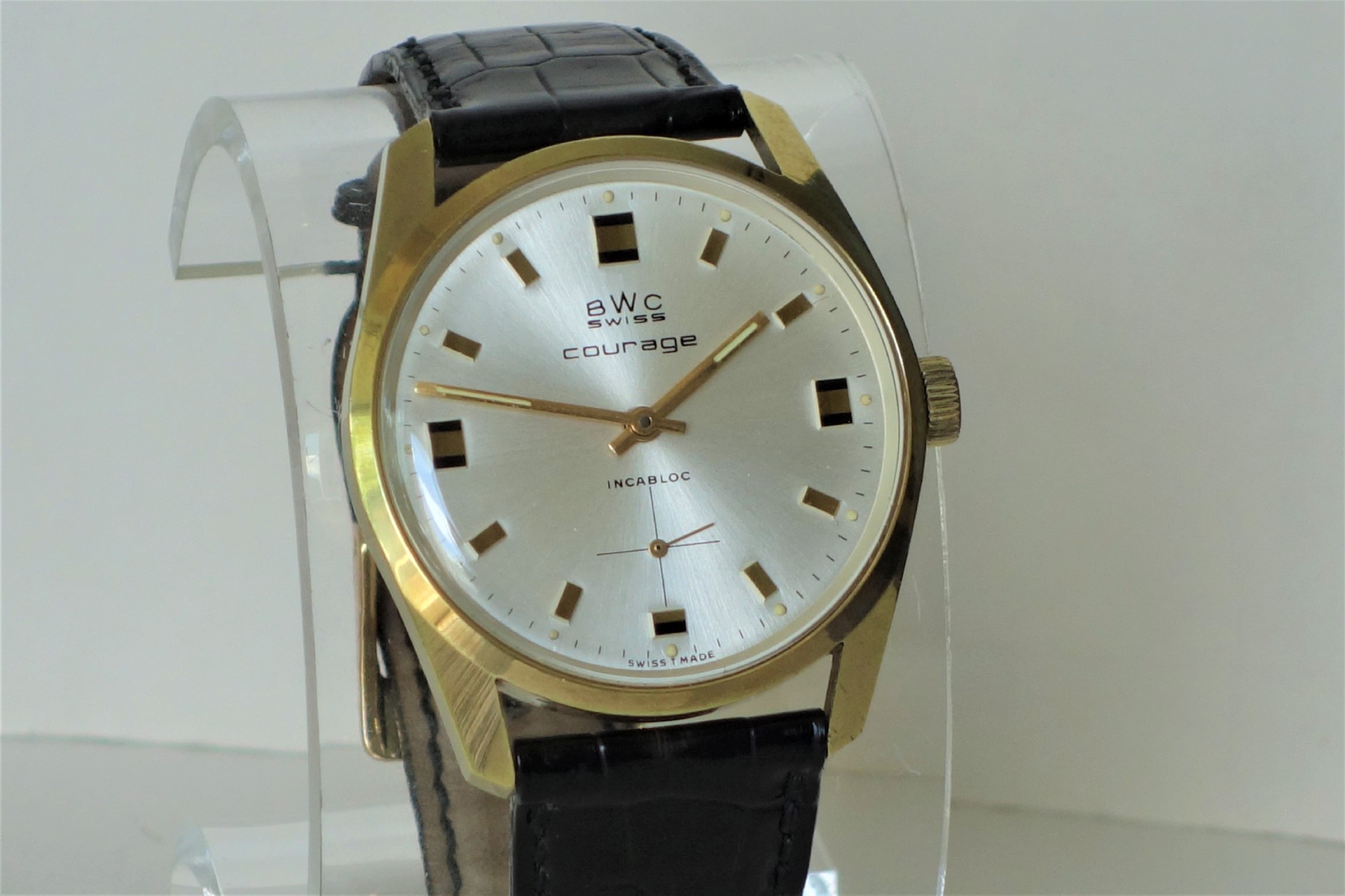 Analoge Armbanduhr mit goldfarbenem Gehäuse, silbernem Zifferblatt und schwarzem Lederarmband.