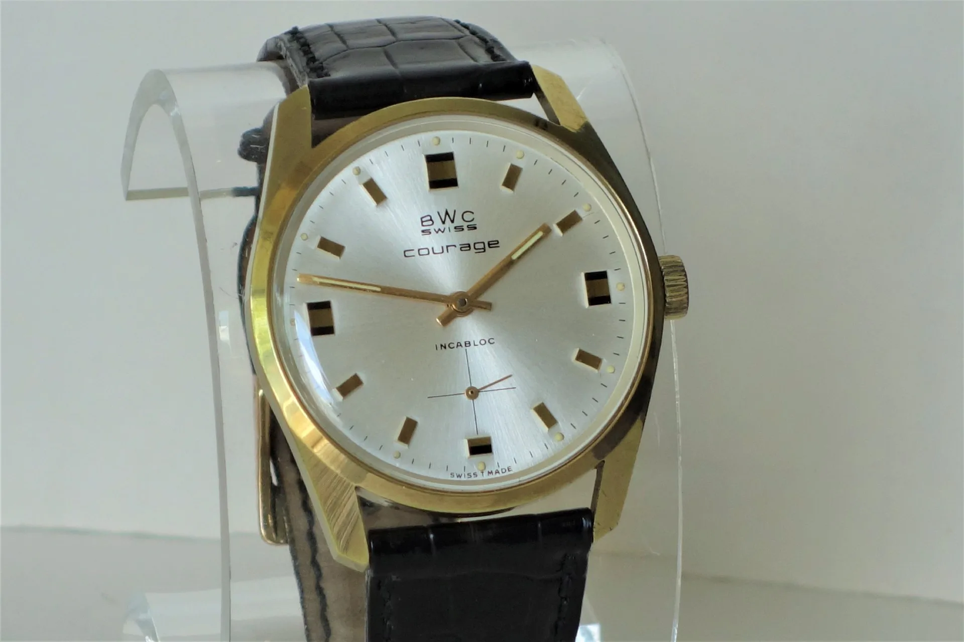 BWC Swiss Armbanduhr Analoge Armbanduhr mit goldfarbenem Gehäuse, silbernem Zifferblatt und schwarzem Lederarmband.