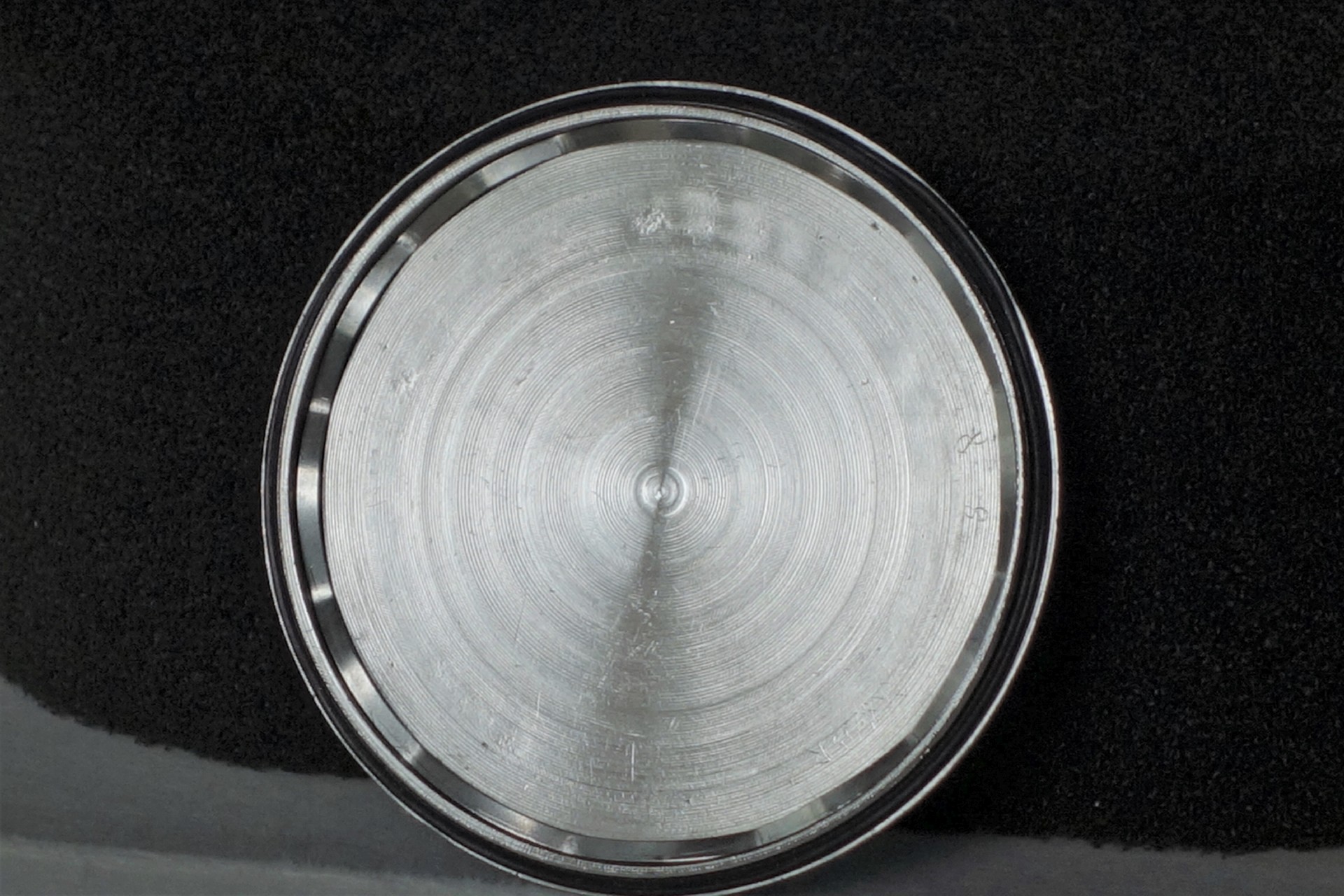 Runder silberfarbener Uhrenboden mit feinen Kreismustern.
