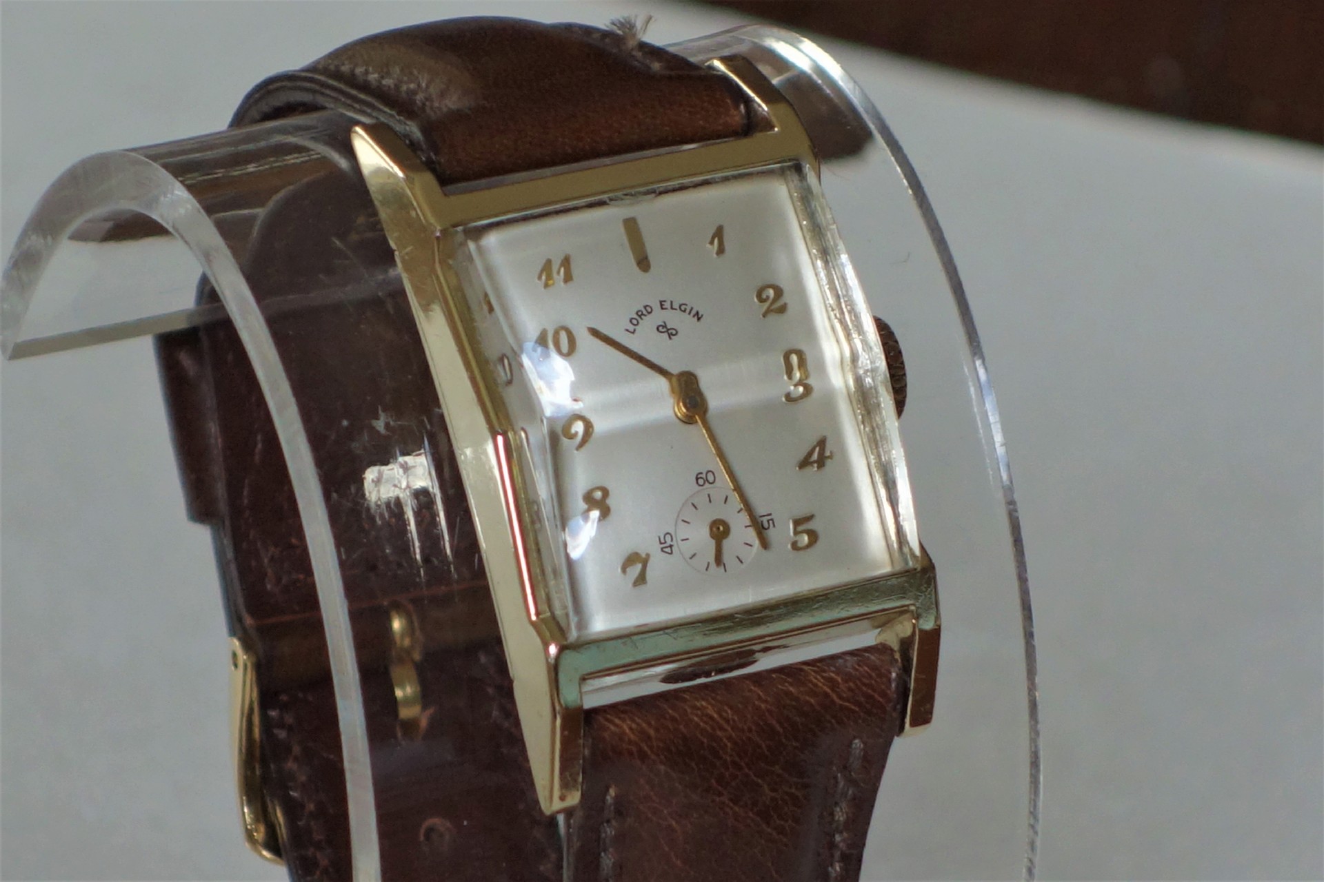 Rechteckige Armbanduhr mit braunem Armband und hellem Zifferblatt.