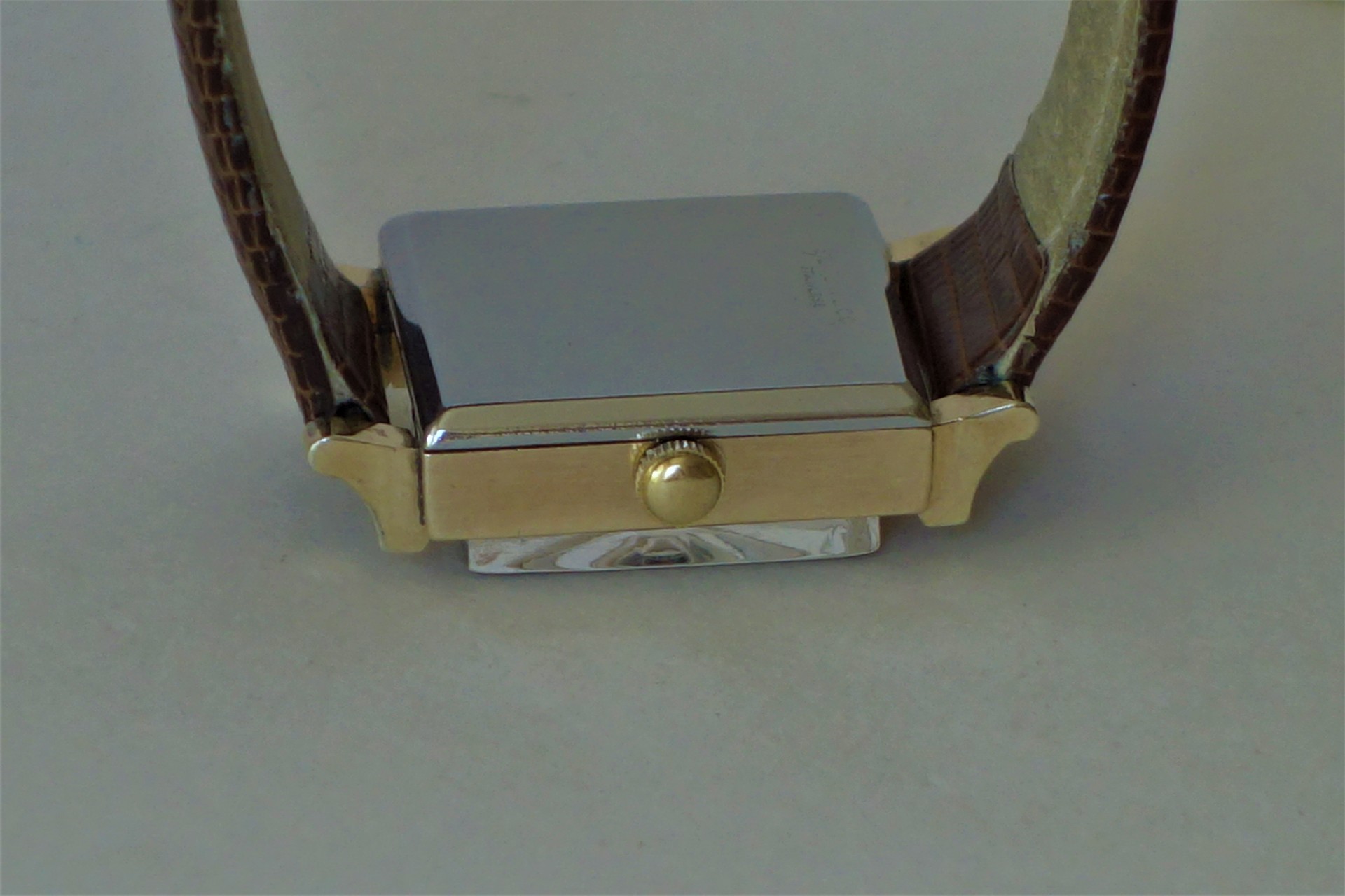 Rechteckiges Uhrengehäuse mit goldfarbenem Rand, silberner Rückseite und braunem Lederarmband.