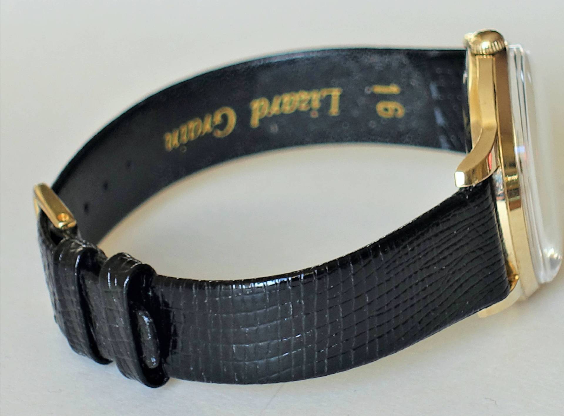 Schwarzes strukturiertes Lederarmband mit goldfarbener Dornschließe an einer Uhr.