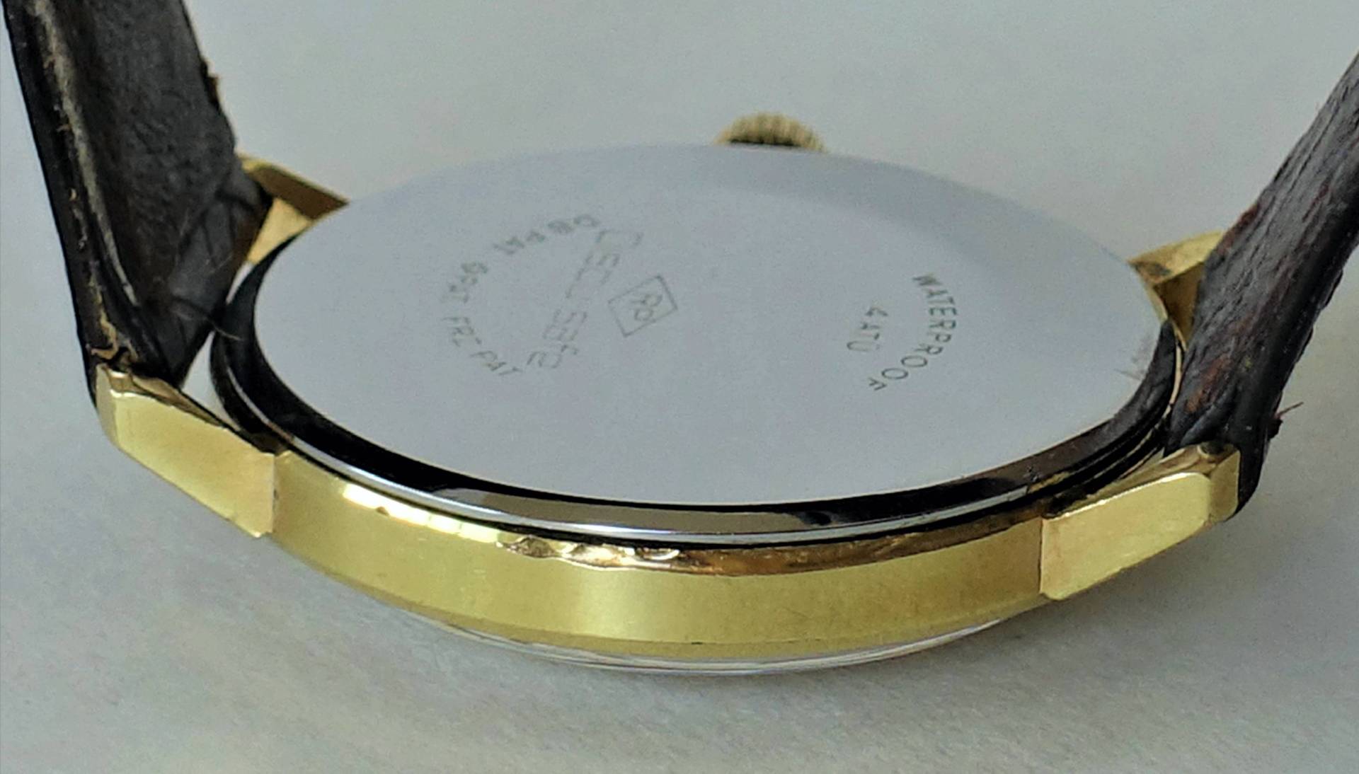Silberfarbener Uhrboden an einem goldfarbenen Uhrengehäuse mit braunem Armband.