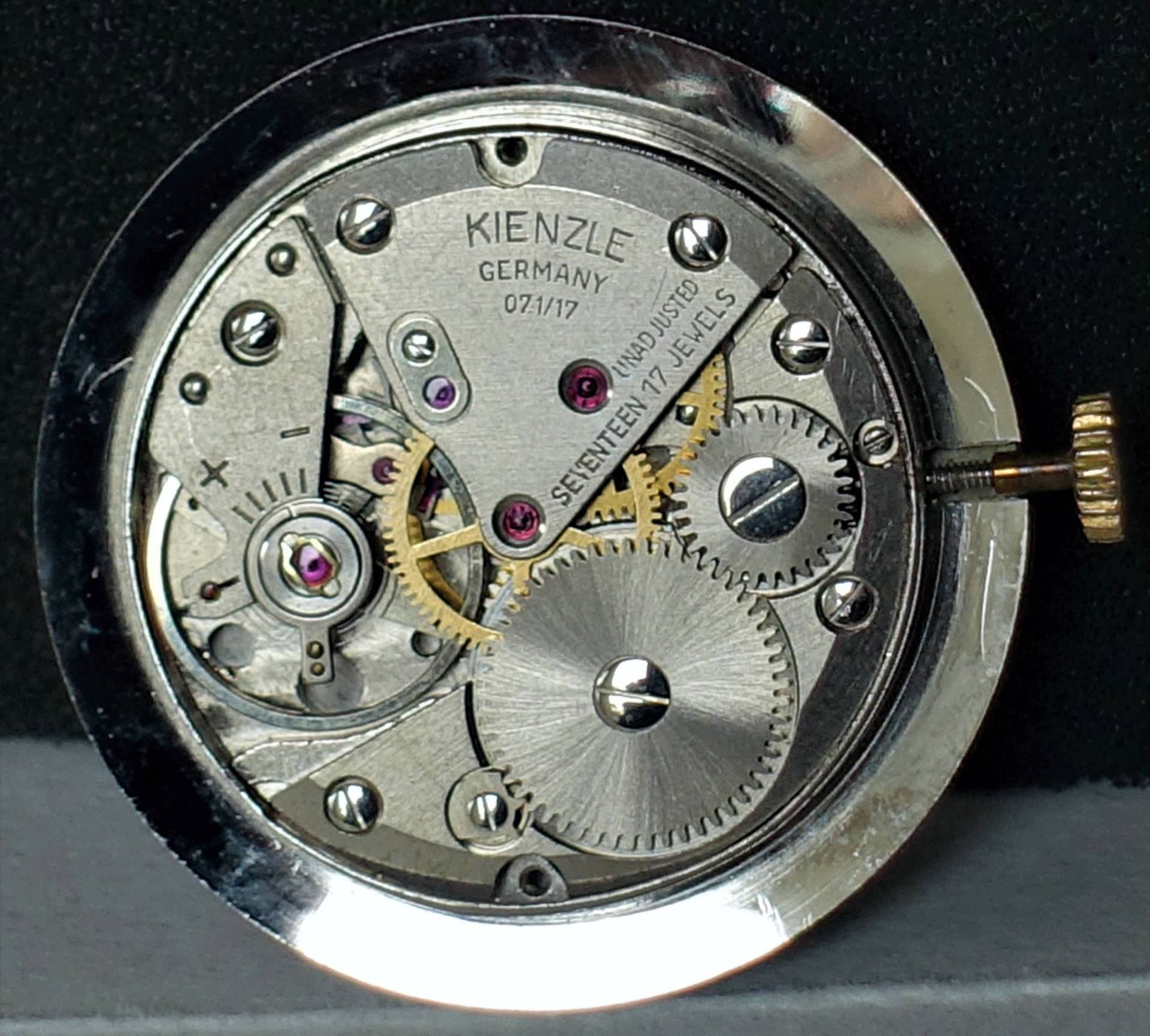 Silberfarbenes mechanisches Uhrwerk von Kienzle mit sichtbaren Zahnrädern und Aufzugswelle.
