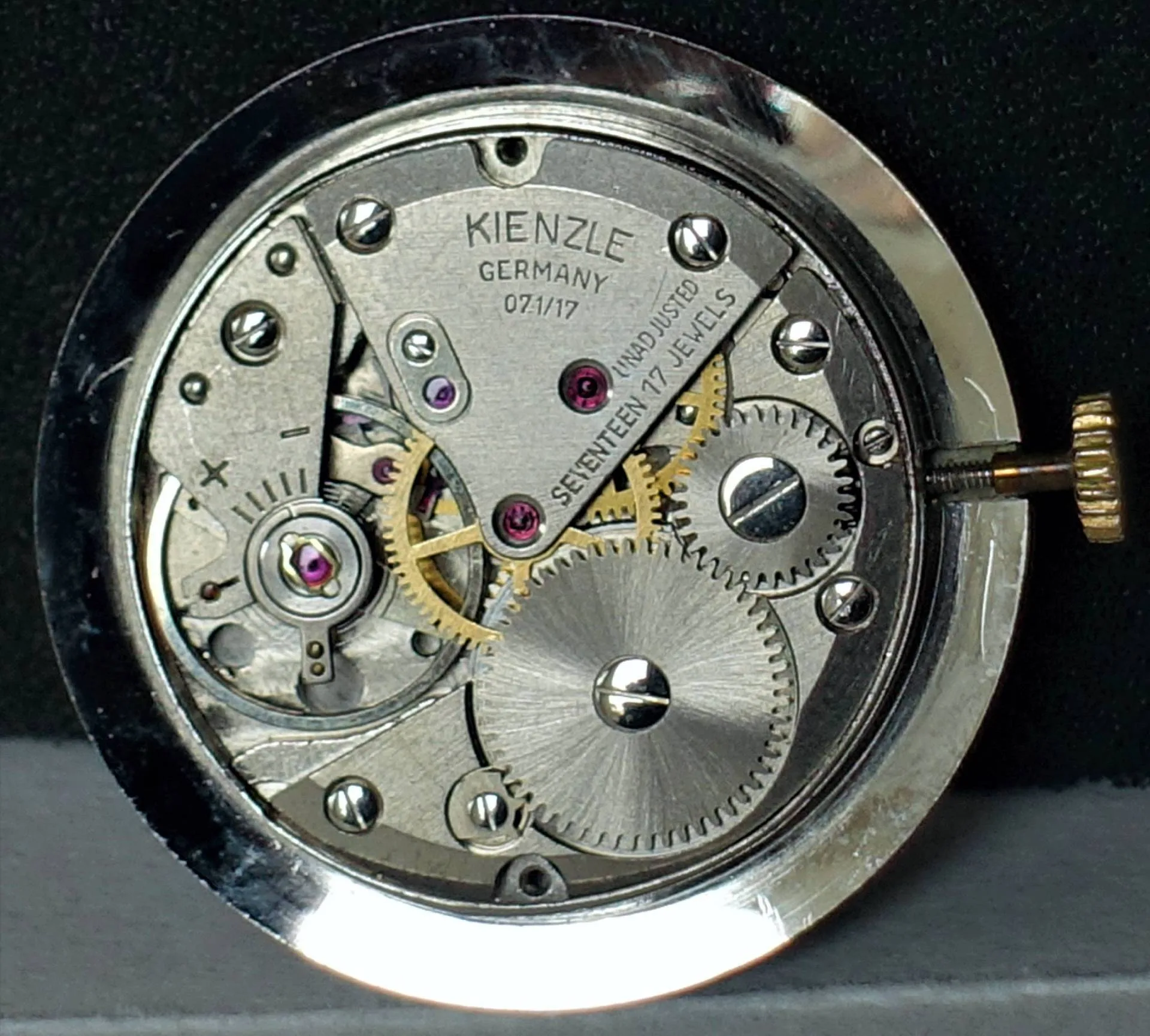Silberfarbenes mechanisches Uhrwerk von Kienzle mit sichtbaren Zahnrädern und Aufzugswelle.