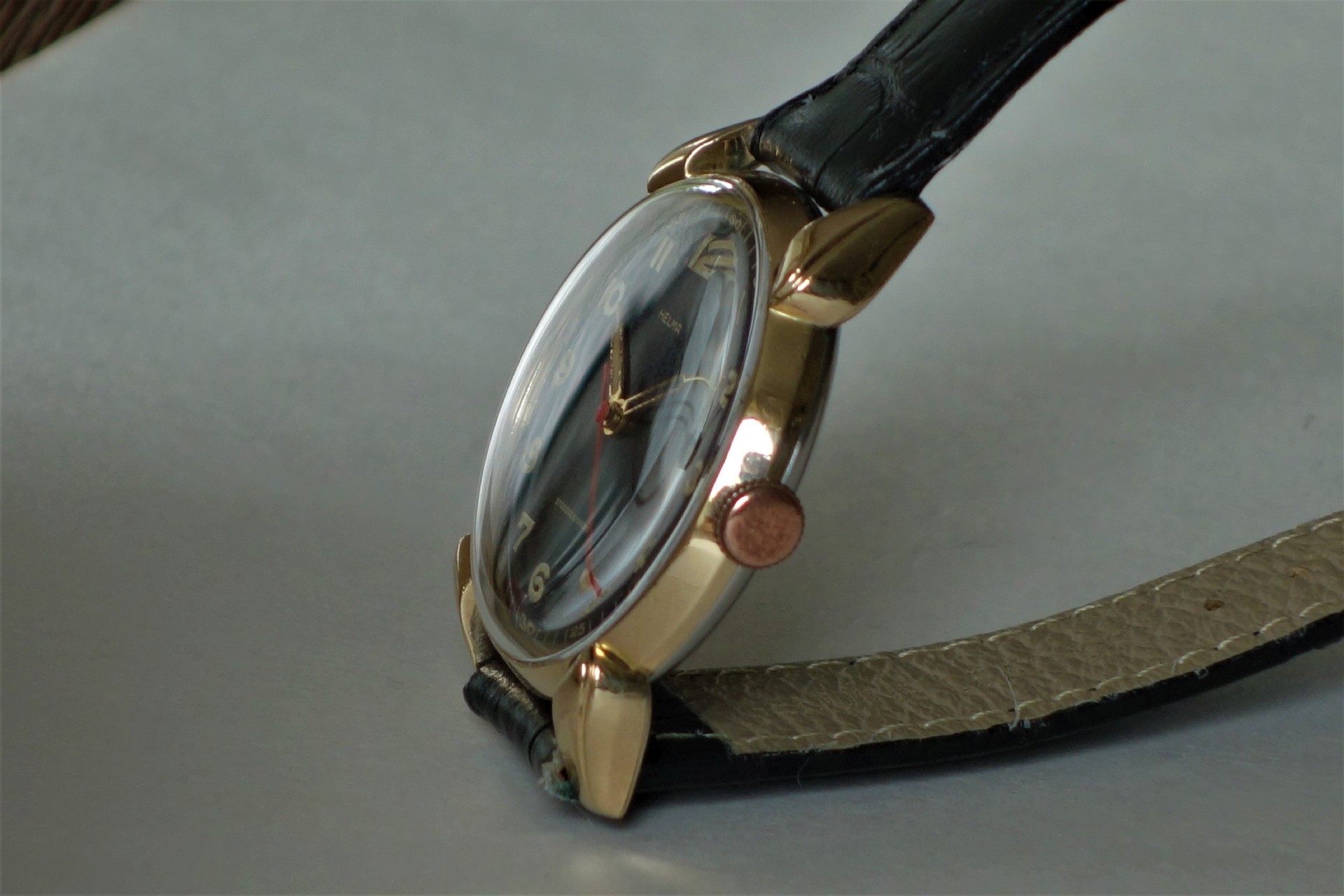 Analoge Armbanduhr mit goldfarbenem Gehäuse, schwarzem Zifferblatt und schwarzem Armband.