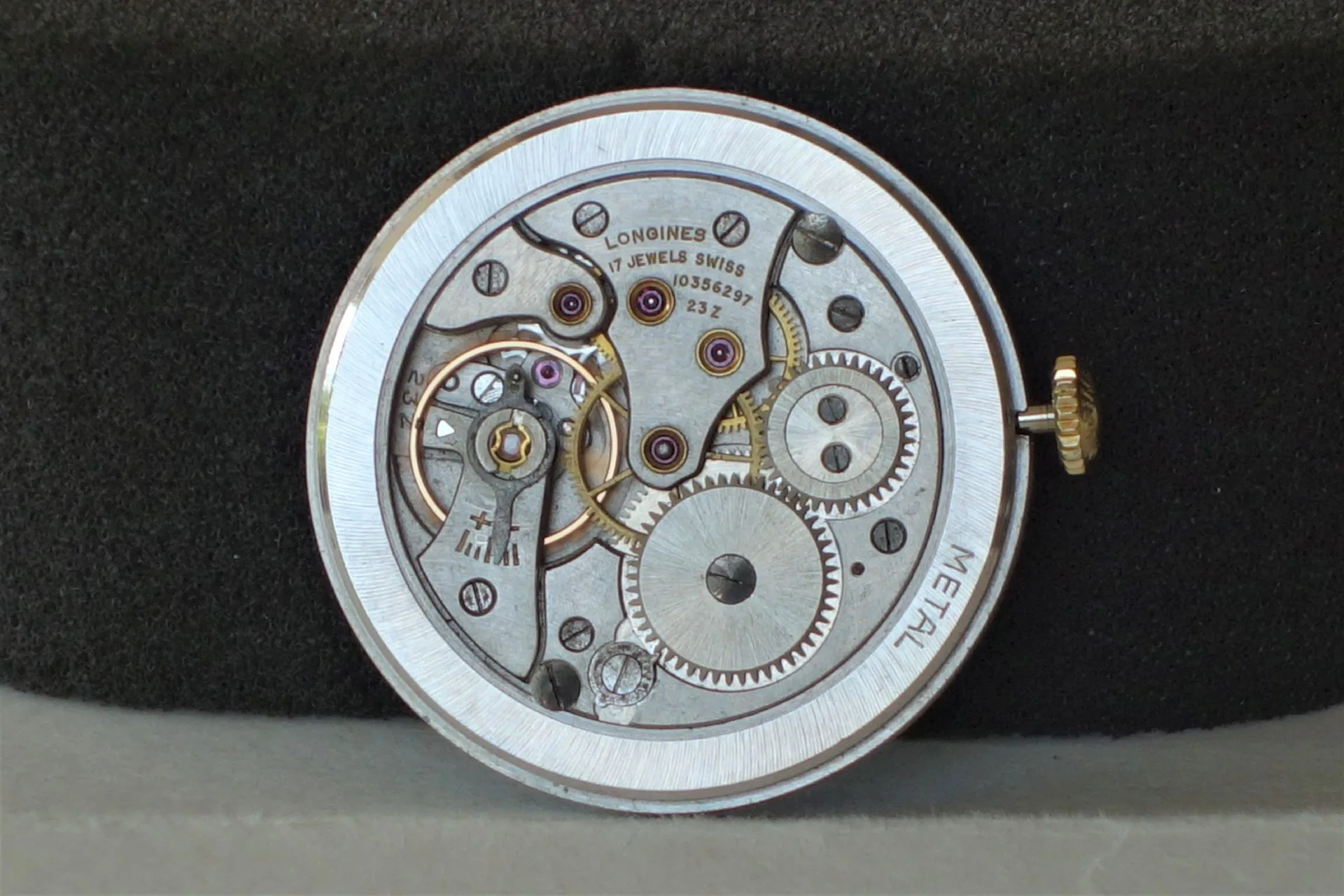 Silberfarbenes mechanisches Uhrwerk von Longines mit sichtbaren Zahnrädern und goldfarbener Krone.