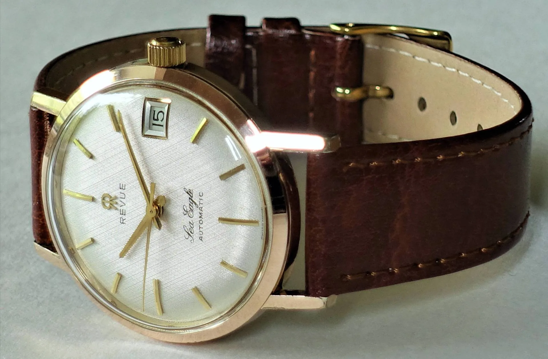 Revue Armbanduhr goldfarben Goldfarbene Armbanduhr mit weißem Zifferblatt und braunem Lederarmband.
