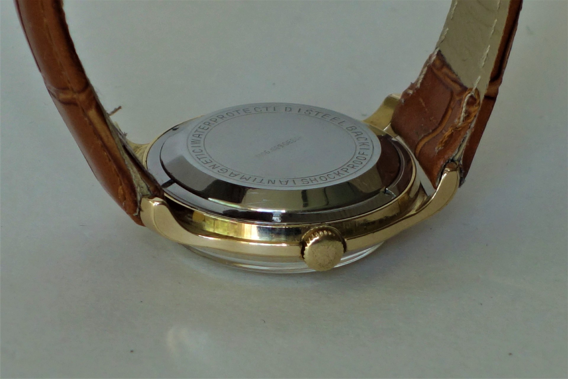 Silberfarbener runder Uhrenboden an einer Uhr mit braunem Armband.